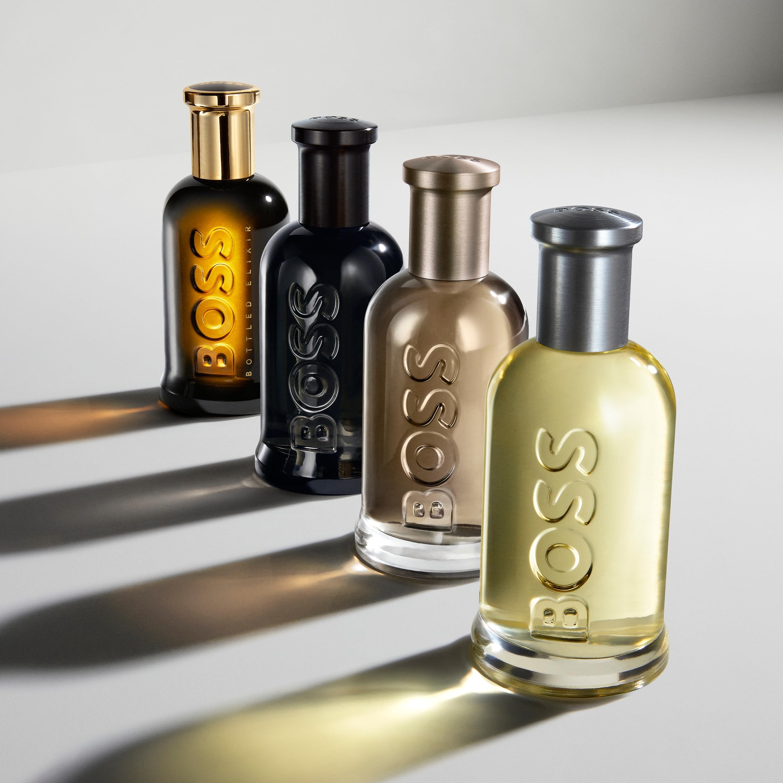 Quatro frascos do perfume Boss Bottled, da Hugo Boss, com design cilíndrico e vidro espesso, dispostos em perspectiva com luz suave refletindo na superfície.