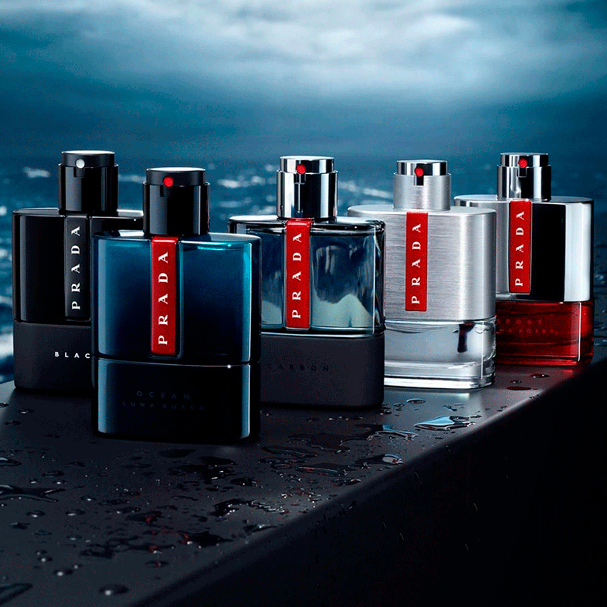 Cinco perfumes da linha Luna Rossa da Prada em tons metálicos e azuis, dispostos sobre superfície molhada com fundo oceânico, transmitindo modernidade e frescor.