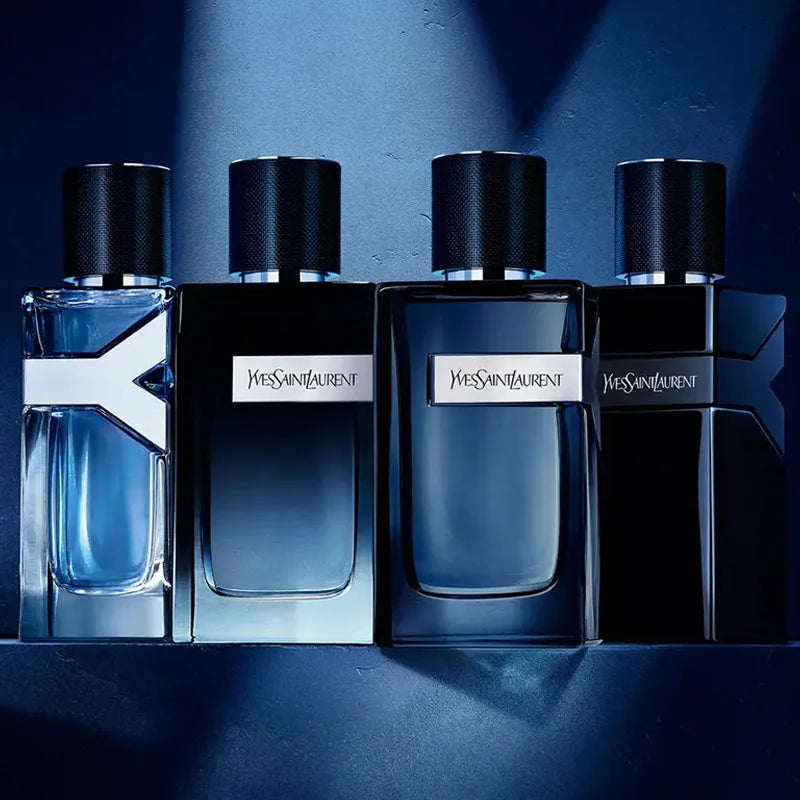 Quatro frascos da linha Y de Saint Laurent em diferentes tons de azul e preto, alinhados sobre fundo escuro com iluminação dramática, revelando sofisticação e mistério.