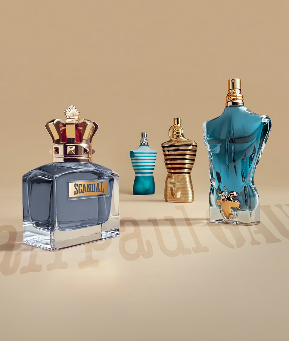 Frascos icônicos da linha masculina da Jean Paul Gaultier, incluindo Scandal e Le Male, com design corporal e detalhes metálicos em fundo bege elegante.