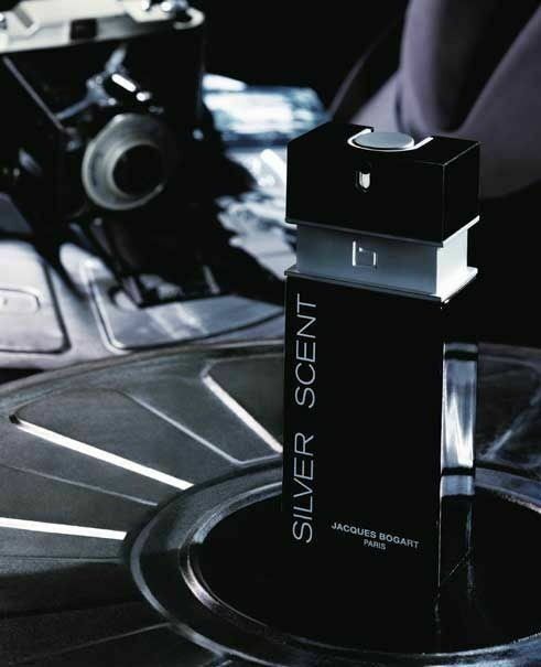 Frasco do perfume Silver Scent, de Jacques Bogart, em destaque sobre uma superfície metálica que remete ao design de rodas automotivas. O frasco preto com detalhes prateados transmite masculinidade, sofisticação e poder, em um cenário urbano e moderno.