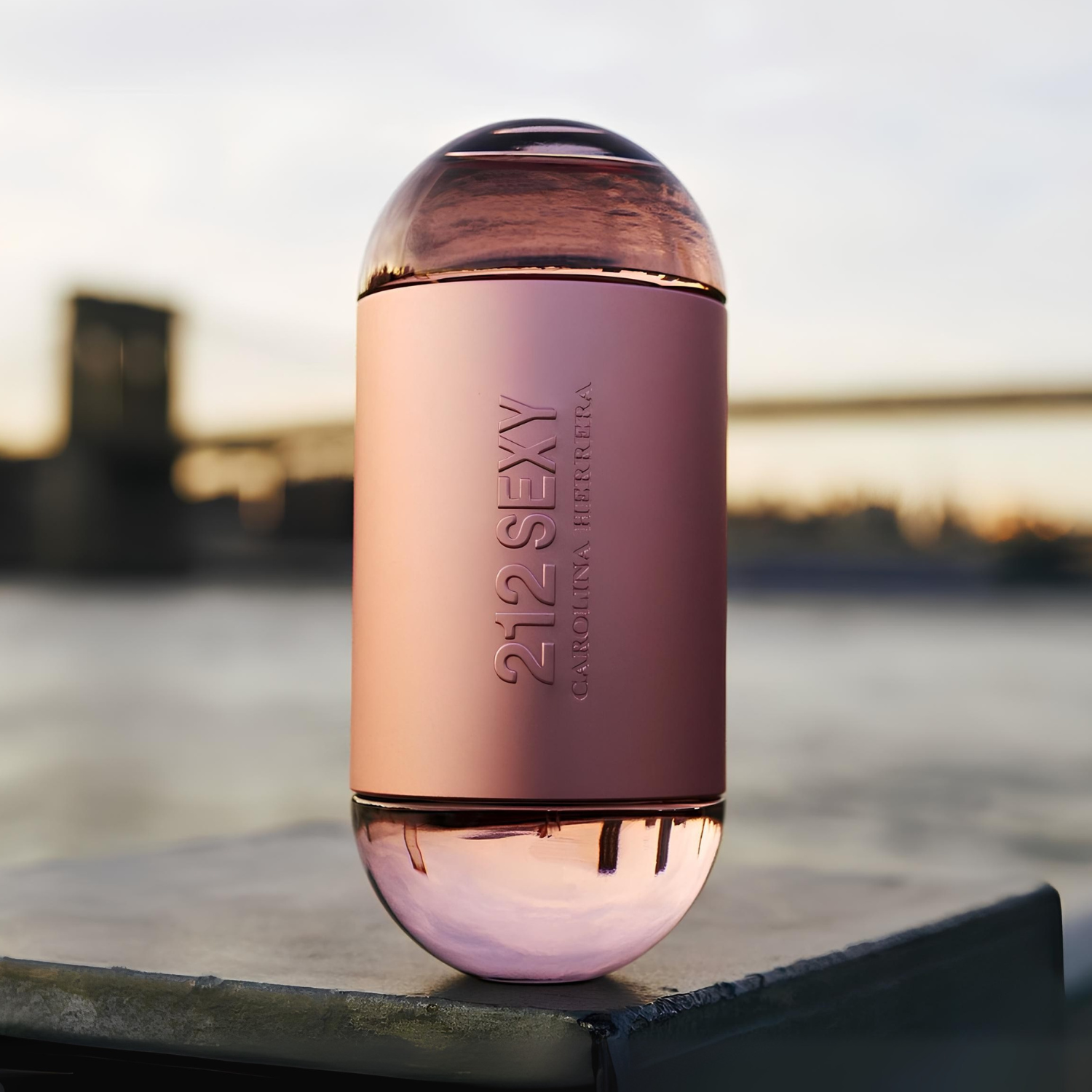 Perfume feminino 212 Sexy Carolina Herrera em destaque sobre uma superfície cinza, com uma paisagem urbana desfocada ao fundo, sugerindo uma fragrância sofisticada e cosmopolita, ideal para a vida noturna na cidade.