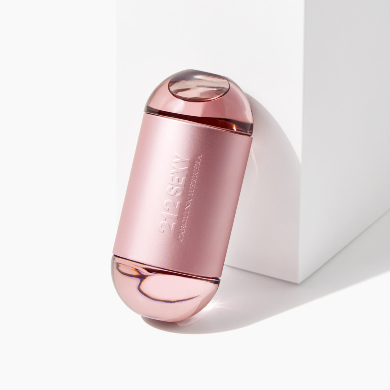 Perfume 212 Sexy Carolina Herrera inclinado sobre uma superfície branca com uma sombra projetada, em um ambiente minimalista que realça o design elegante e sensual do frasco.