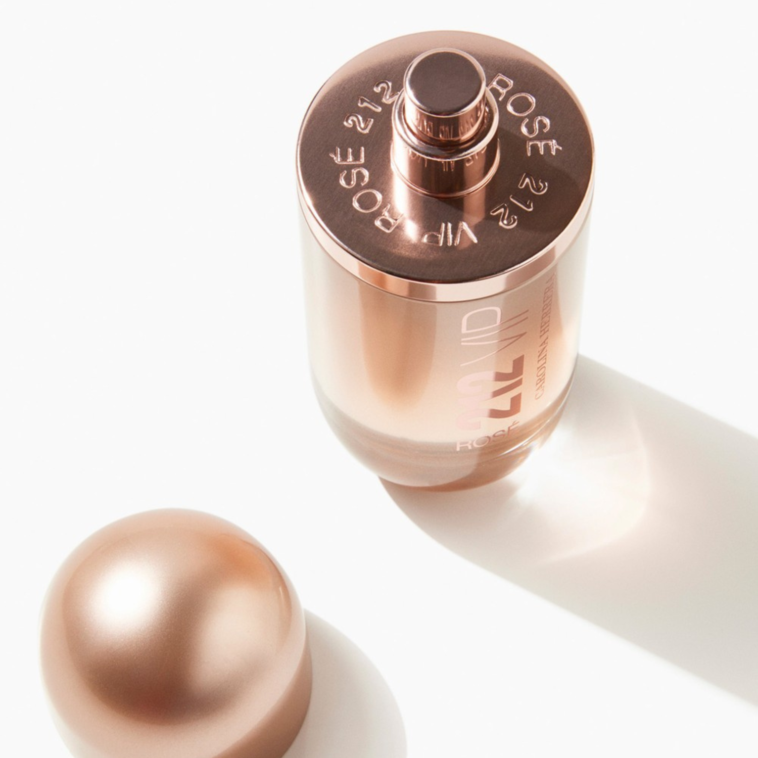 Vista superior do perfume 212 VIP Rosé Carolina Herrera com a tampa removida ao lado, mostrando o borrifador dourado e a inscrição "212 VIP ROSÉ CAROLINA HERRERA" circular na parte superior do frasco, enfatizando os detalhes do design e a marca.