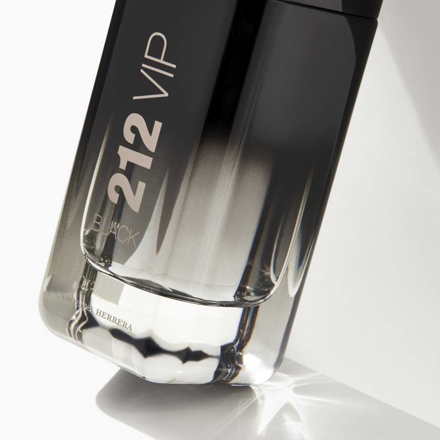 Close-up da base do perfume importado masculino 212 VIP Black Carolina Herrera, realçando o degradê do frasco, o líquido e o logotipo da marca na parte inferior transparente, disponível na Velyre.