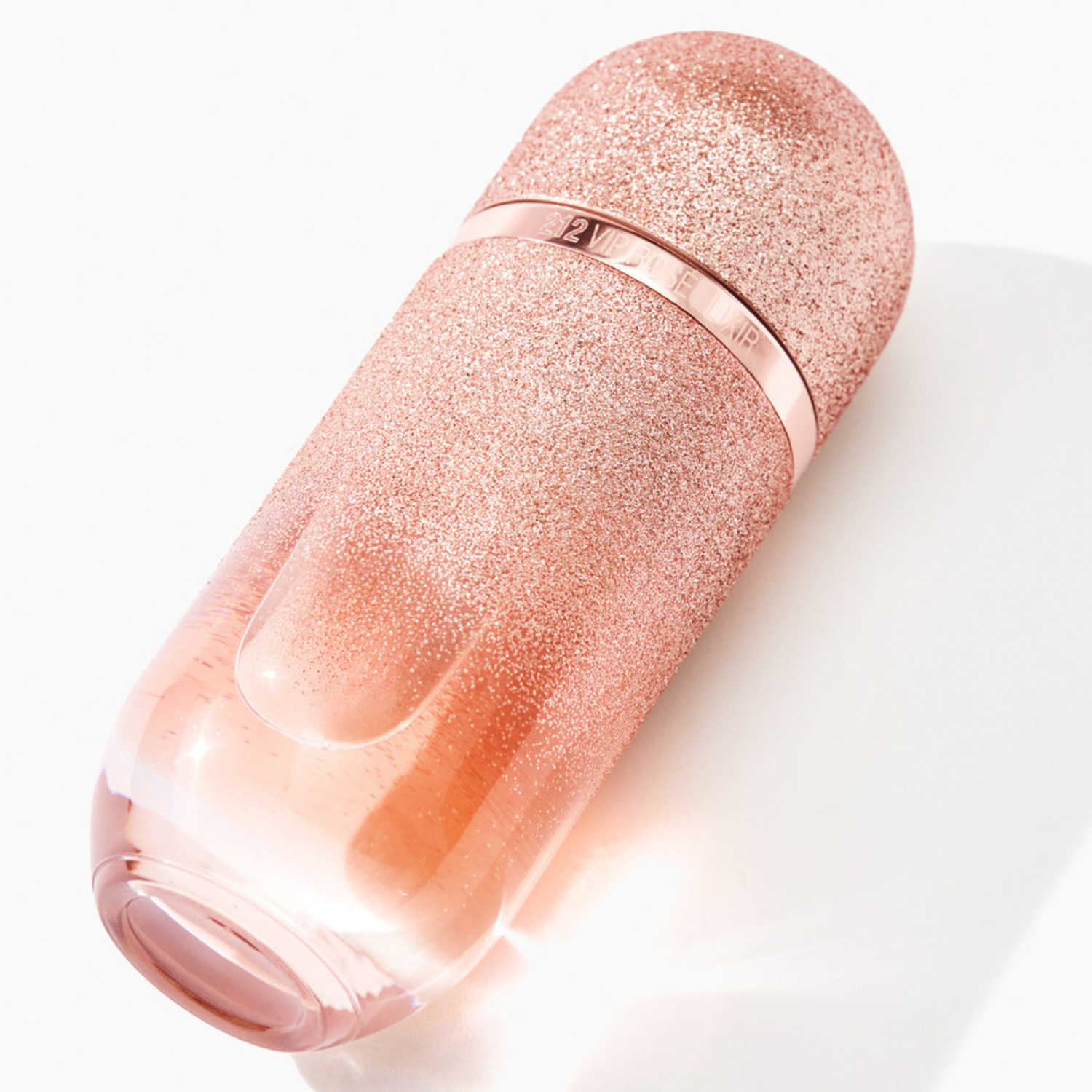 Perfume importado feminino 212 Vip Rosé Elixir Carolina Herrera inclinado sobre uma superfície clara, realçando o brilho do glitter rose gold do frasco e a cor delicada do líquido rosado, disponível na Velyre.