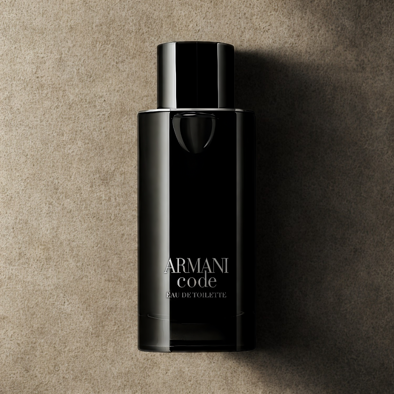 Perfume masculino Armani Code Giorgio Armani em destaque sobre uma superfície texturizada em tons de bege e marrom, realçando o design sofisticado e minimalista do frasco preto.