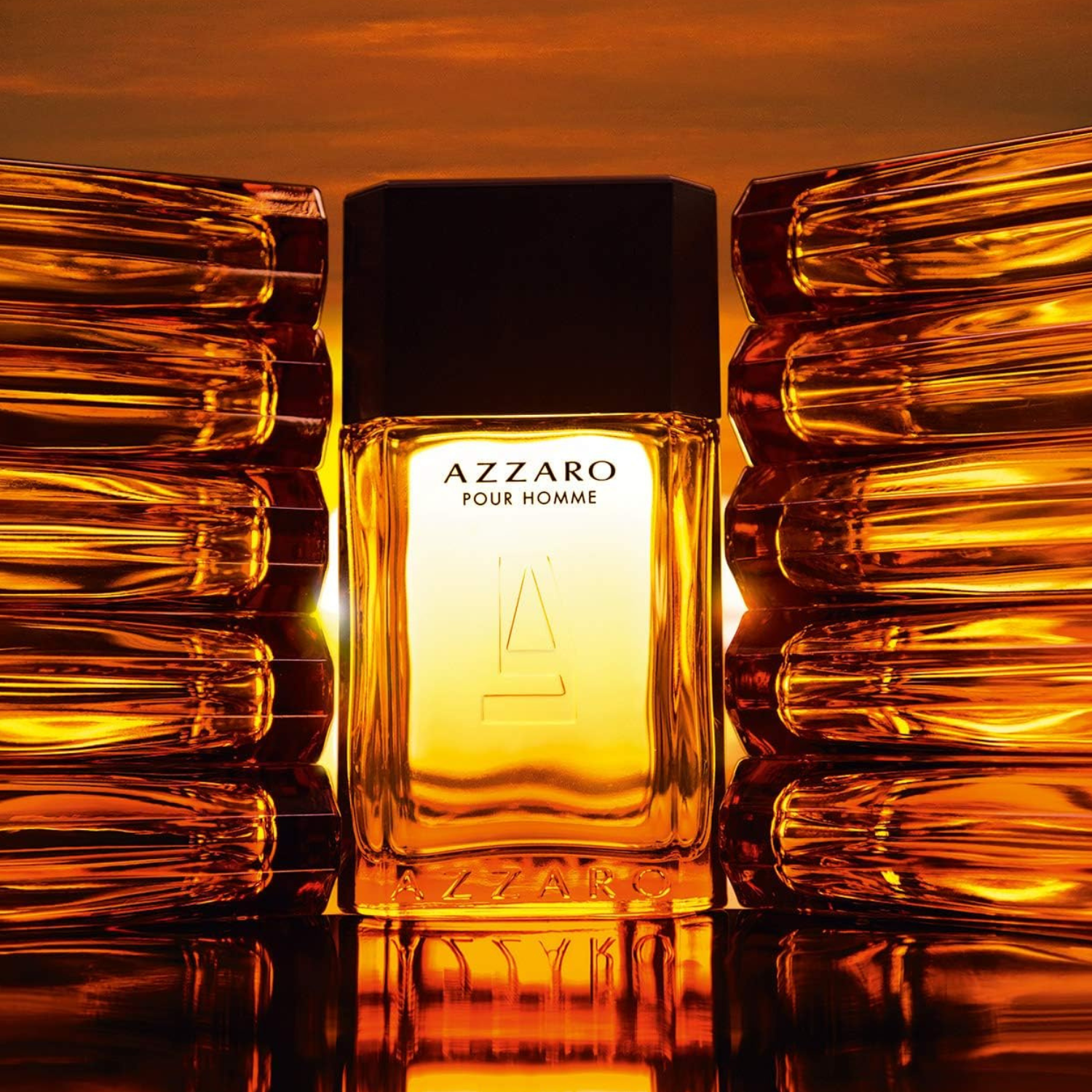 Perfume Azzaro Pour Homme entre frascos âmbar refletindo luz dourada. O frasco central brilha intensamente com a luz do pôr do sol ao fundo, destacando seu design clássico.