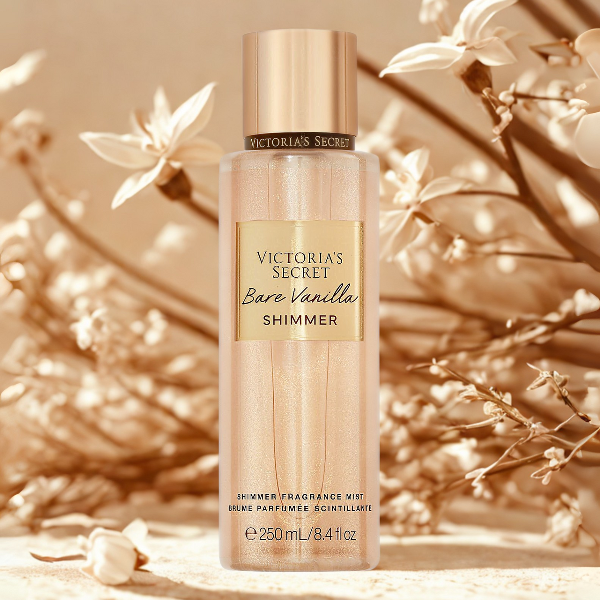 Frasco do body splash importado Bare Vanilla Shimmer Victoria's Secret em destaque em um ambiente delicado com flores brancas e folhagens secas ao fundo, evocando uma fragrância doce, aconchegante e luminosa, disponível na Velyre.