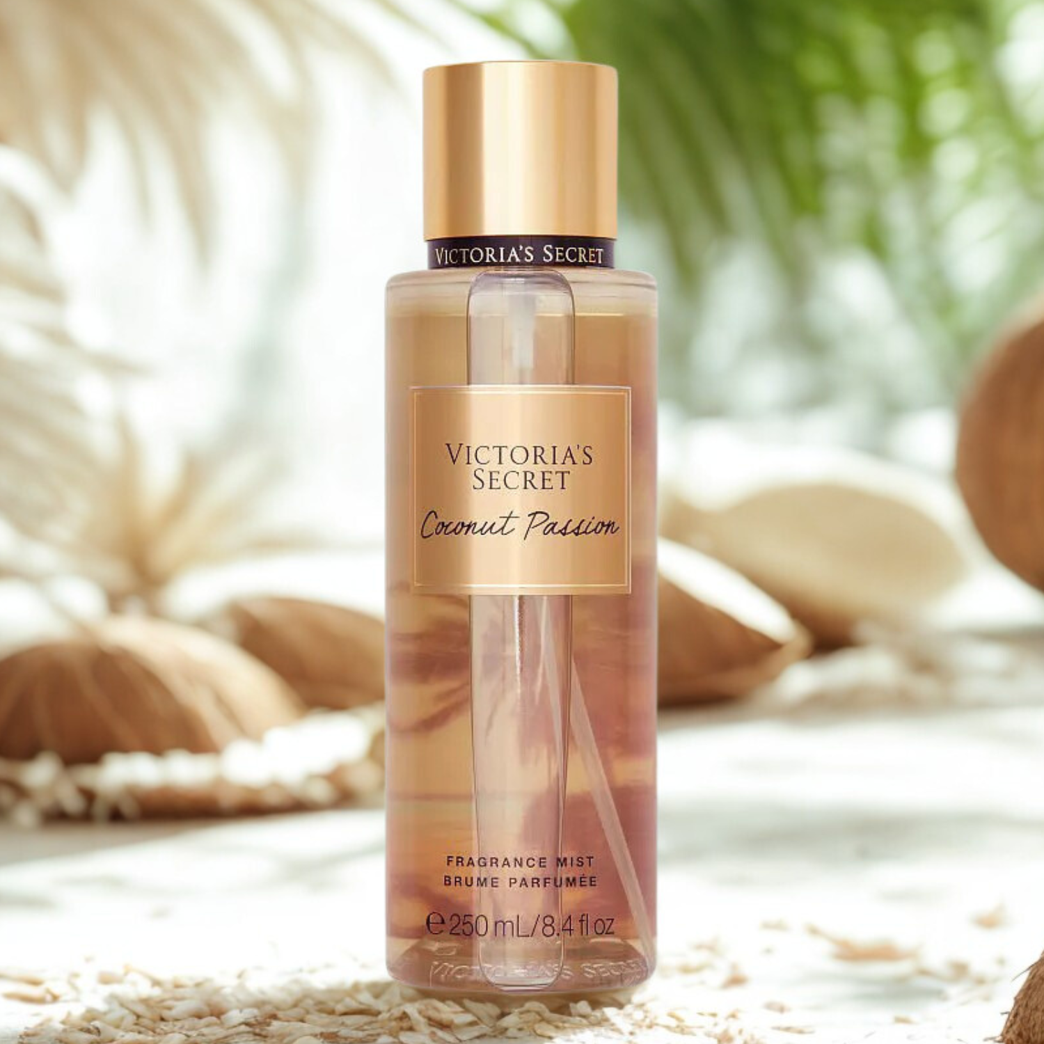 Frasco do body splash importado Coconut Passion Victoria's Secret em destaque em um ambiente tropical com folhas secas e elementos que remetem a casca de coco, evocando uma fragrância exótica e quente, disponível na Velyre.