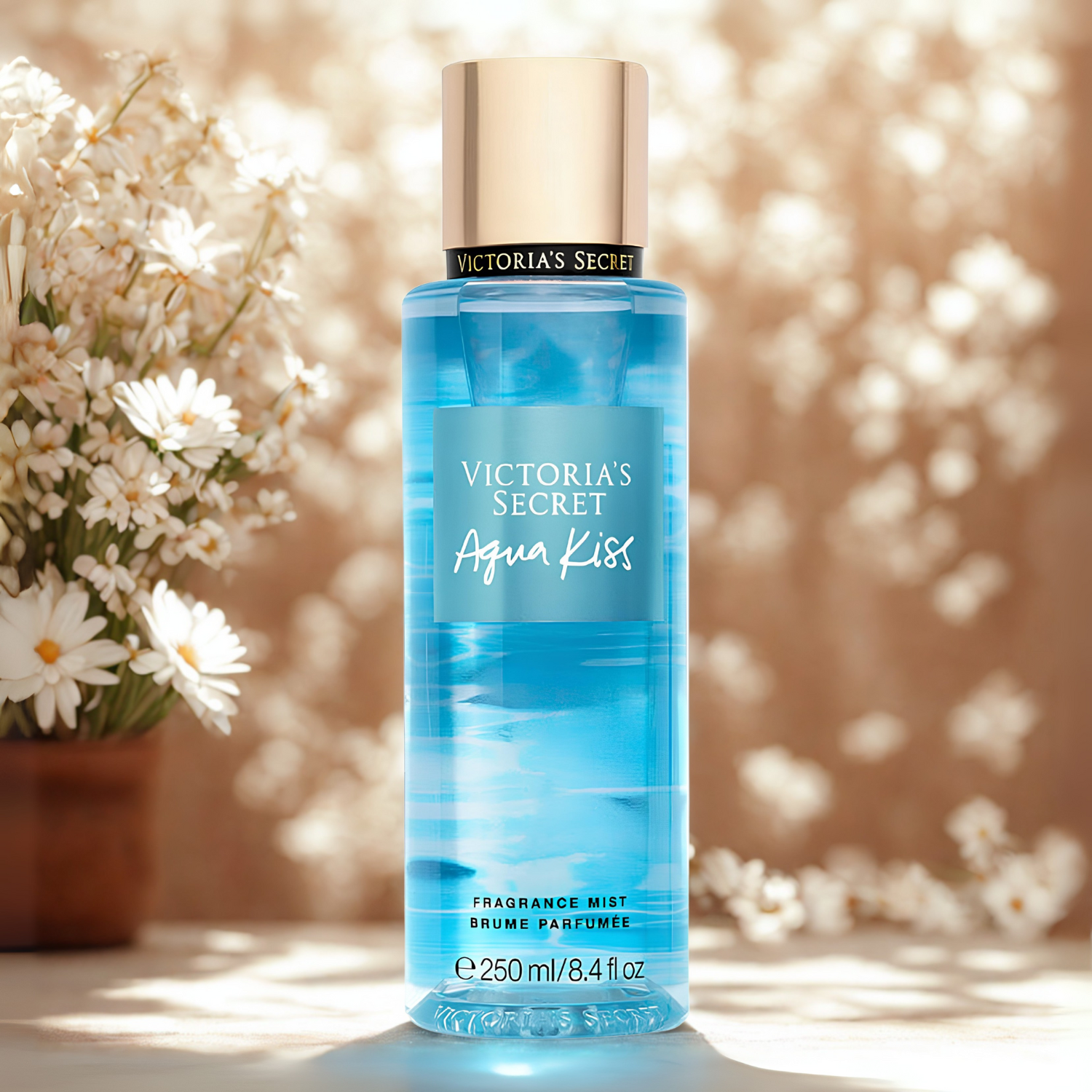 Frasco do body splash importado Acqua Kiss Victoria's Secret em destaque em um ambiente fresco com flores brancas e um fundo desfocado, evocando uma fragrância aquática e floral, disponível na Velyre.