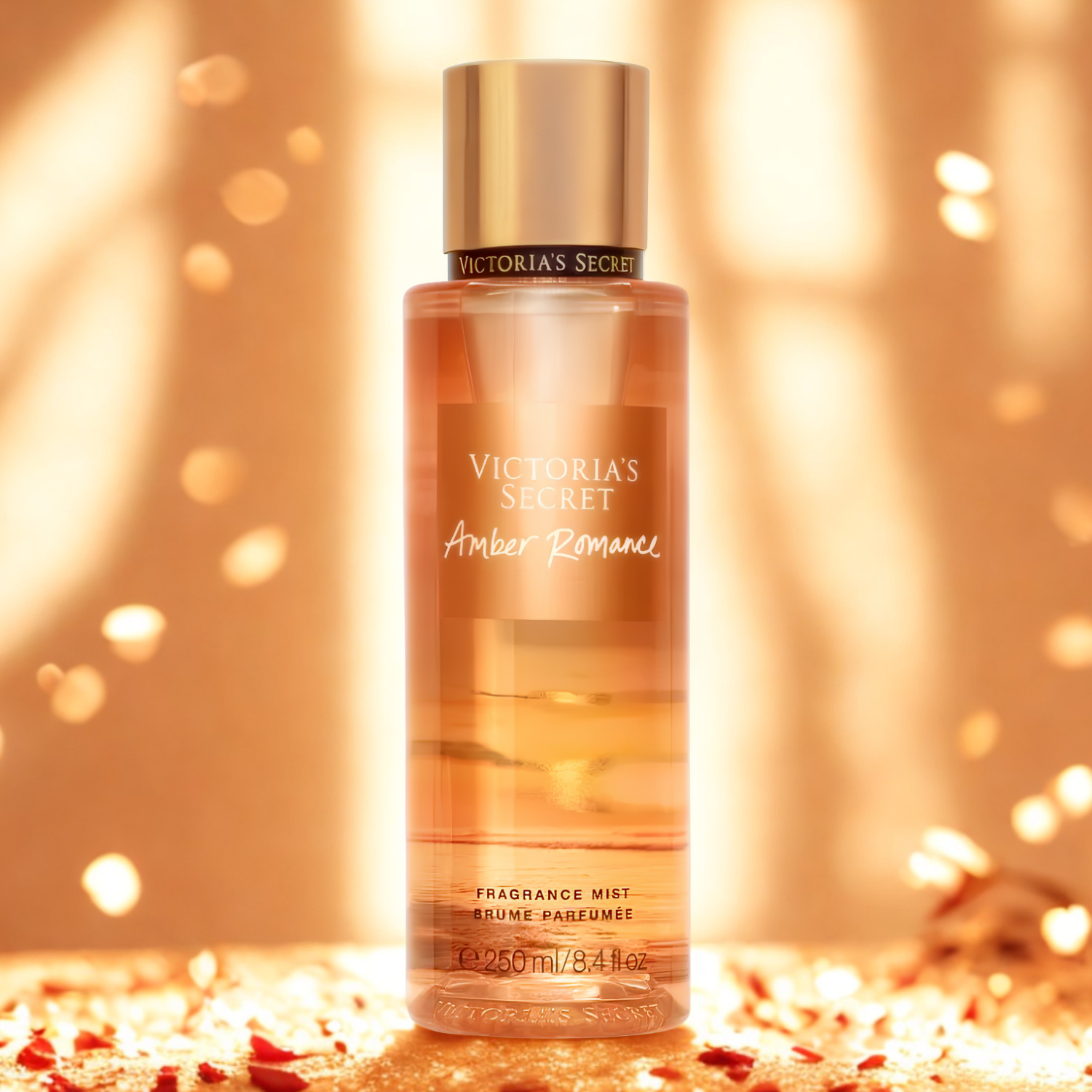 Frasco do body splash importado Amber Romance Victoria's Secret em destaque em um ambiente com brilhos dourados e pequenas pétalas vermelhas espalhadas, evocando uma fragrância quente e sensual, disponível na Velyre.