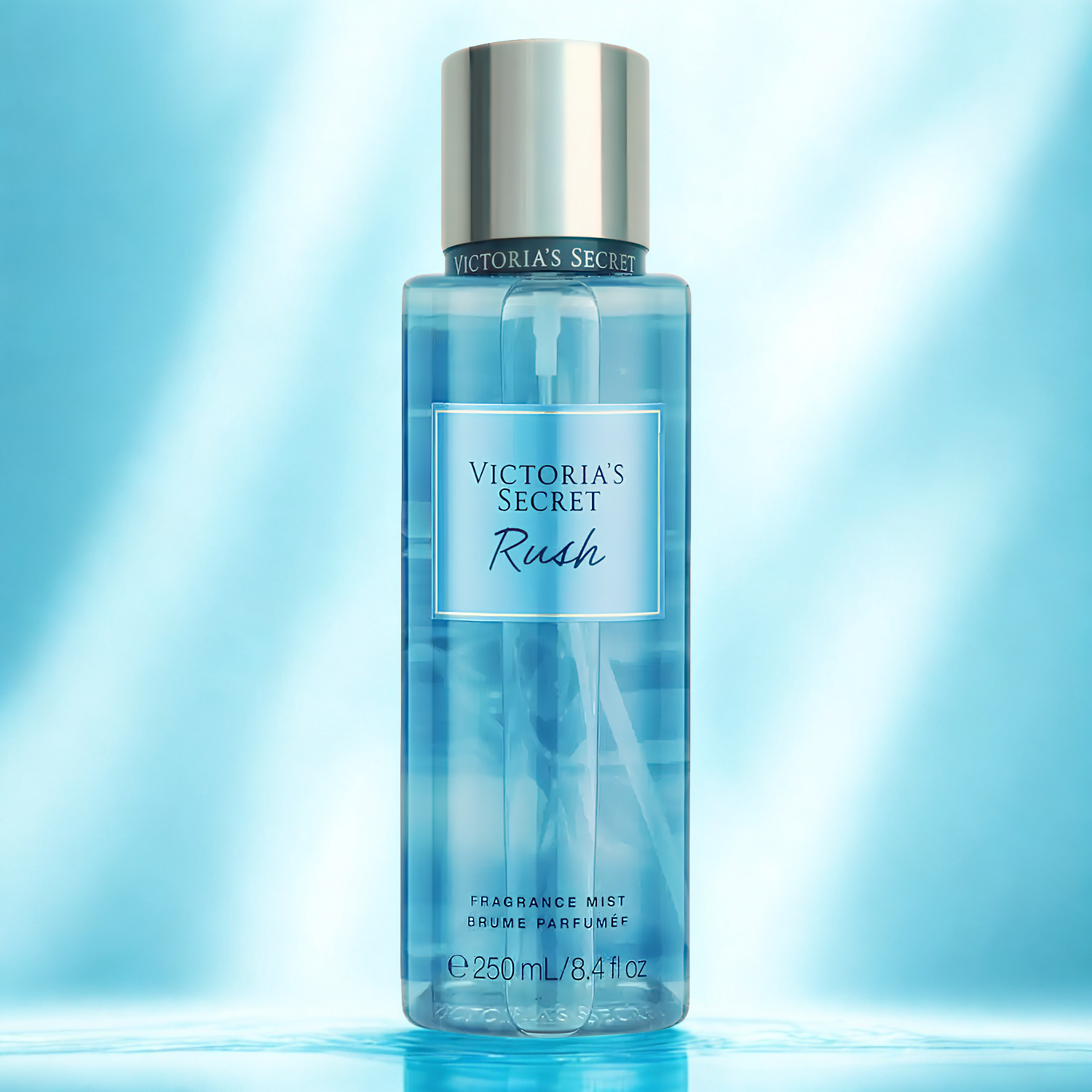Frasco do body splash importado Rush Victoria's Secret em destaque em um ambiente com fundo azul claro e reflexos, evocando uma fragrância fresca e energizante, disponível na Velyre.