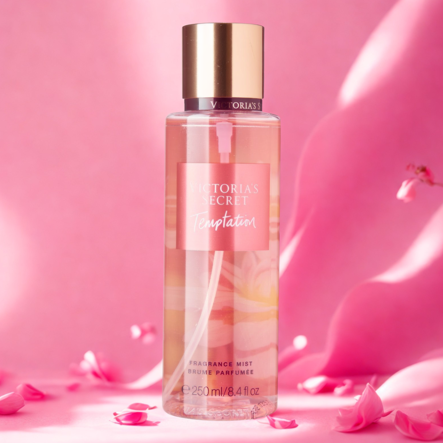 Frasco do body splash importado Temptation Victoria's Secret em destaque em um ambiente romântico com fundo rosa suave e pétalas espalhadas, evocando uma fragrância floral frutada e sedutora, disponível na Velyre.