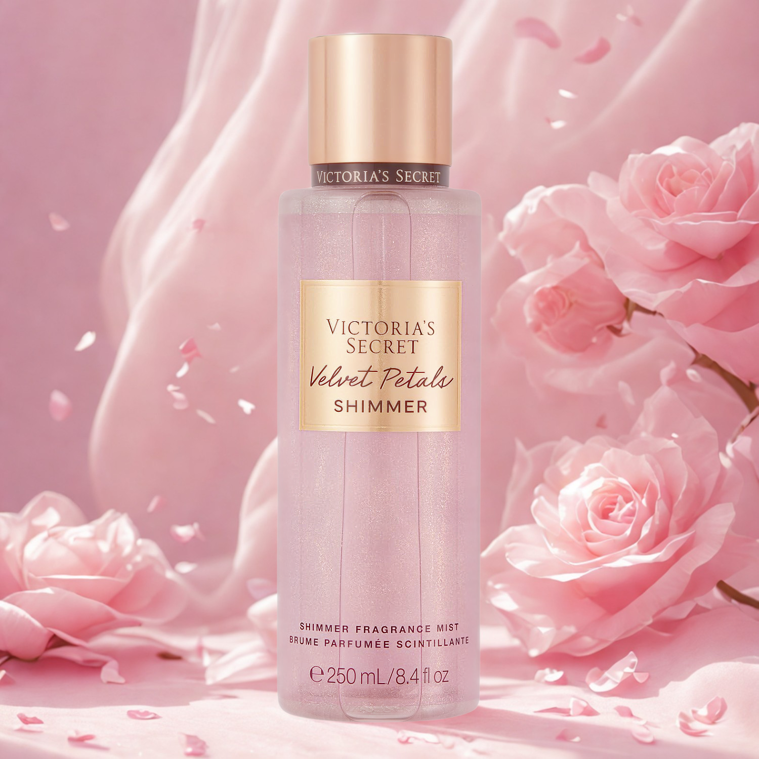 Frasco do body splash importado Velvet Petals Shimmer Victoria's Secret em destaque em um ambiente romântico com volumosas flores cor-de-rosa e brilhos cintilantes ao fundo, evocando uma fragrância floral suave e luminosa, disponível na Velyre.