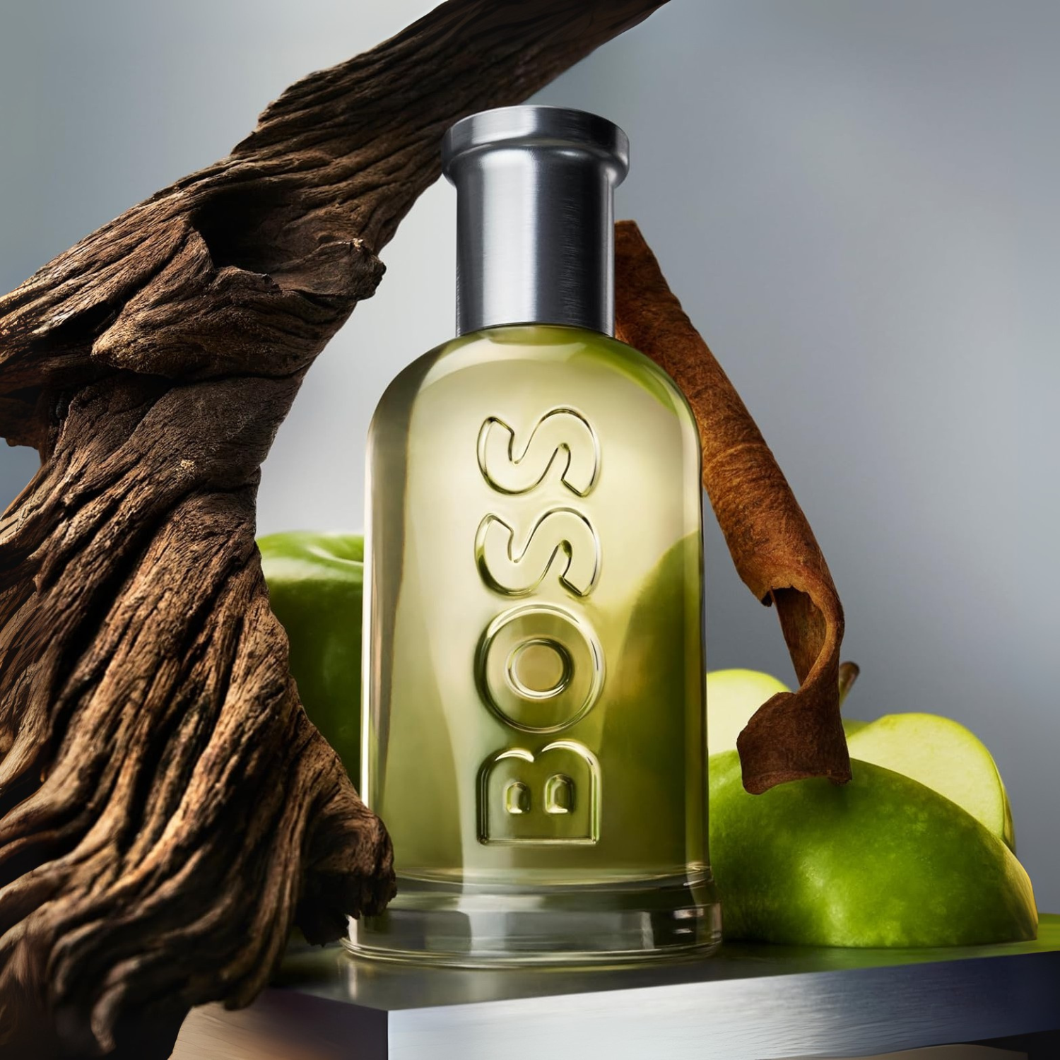 Frasco do Boss Bottled Hugo Boss Eau de Toilette ao lado de maçãs verdes, canela e madeira, destacando suas notas olfativas principais.