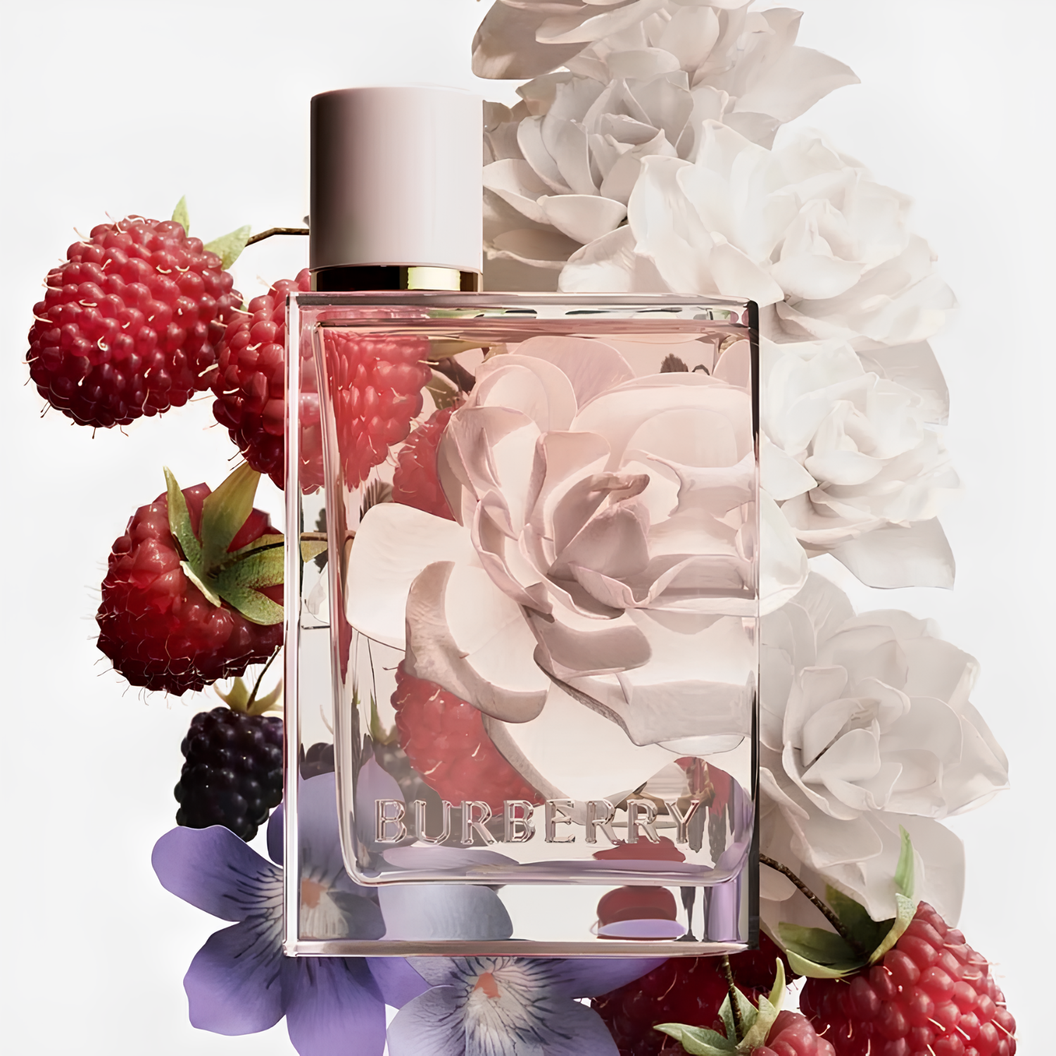 Frasco Burberry Her posicionado diante de flores brancas e frutas vermelhas como framboesas e amoras, simbolizando notas florais e frutadas do perfume. A tampa rosa e o design translúcido refletem feminilidade e sofisticação.