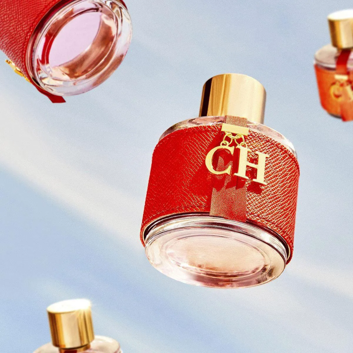 Múltiplos frascos do perfume CH Femme Carolina Herrera caindo contra um céu azul claro, transmitindo uma sensação de leveza e dinamismo.