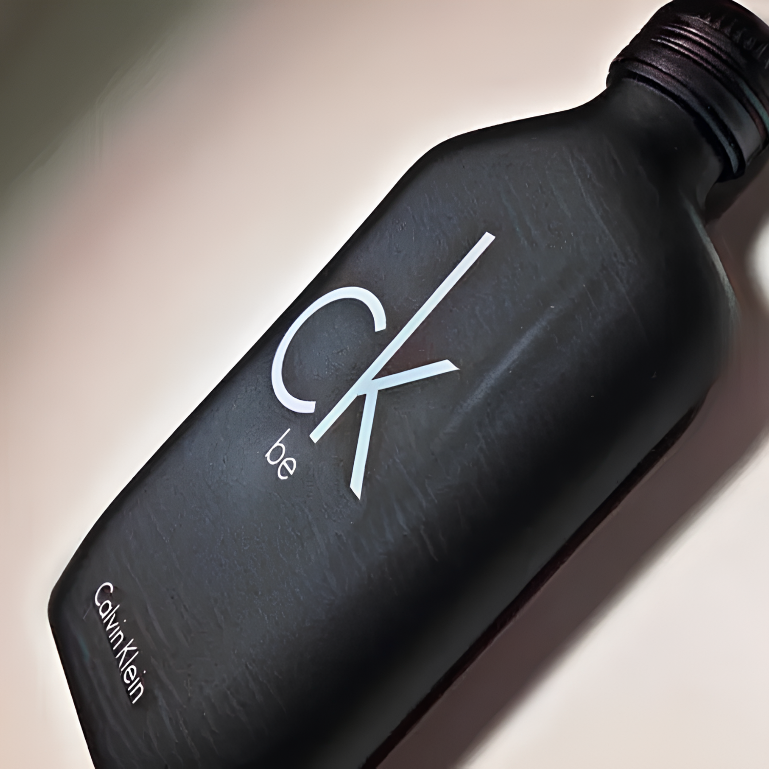Close-up do perfume CK Be Calvin Klein em ângulo, realçando a textura fosca do frasco preto e o logo "ck be" em branco, transmitindo uma estética moderna e discreta.