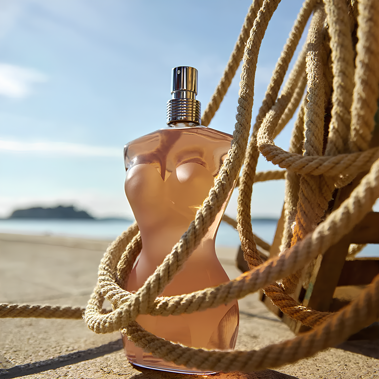 Frasco do perfume Classique Jean Paul Gaultier em ambiente externo, parcialmente envolvido por uma corda grossa, com o mar e o céu azul ao fundo.