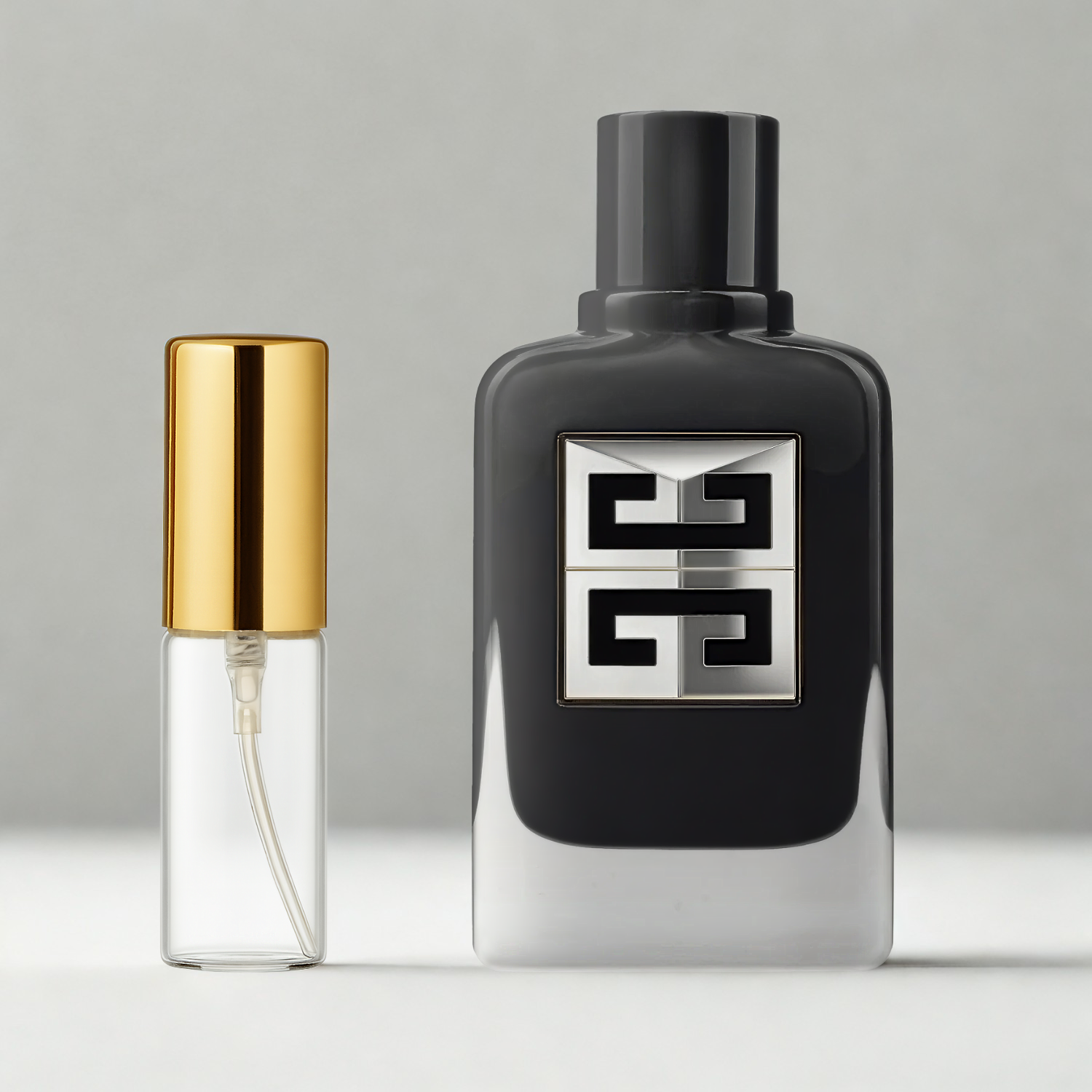 Decant de 5ml com borrifador dourado ao lado do frasco original do perfume importado masculino Gentleman Society Givenchy Eau de Parfum, ambos sobre uma superfície e fundo cinza claro. A imagem destaca a apresentação do decant para venda e a familiaridade com o frasco original, disponíveis na Velyre.