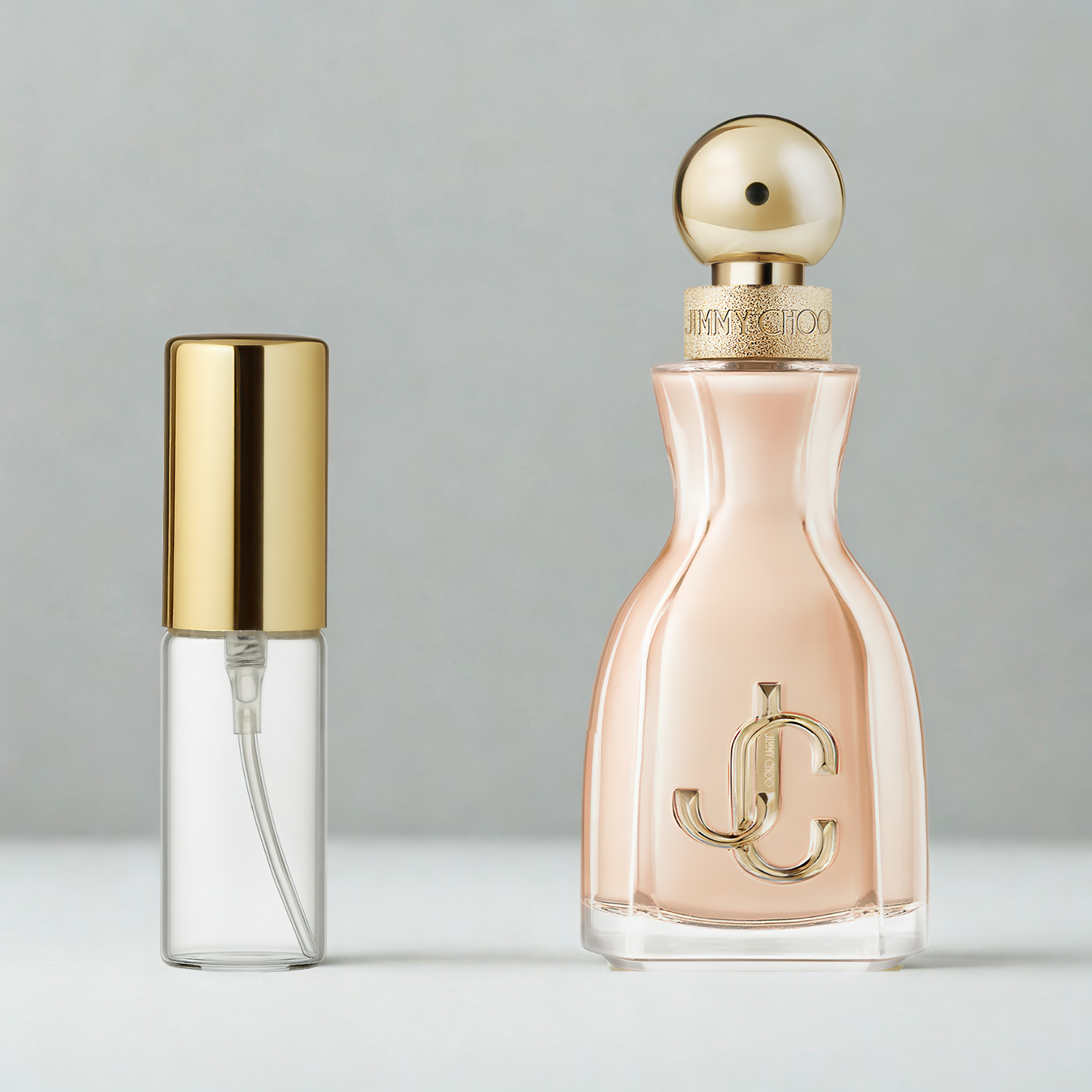 Decant de 5ml com borrifador dourado ao lado do frasco original do perfume importado feminino I Want Choo Jimmy Choo Eau de Parfum, ambos sobre uma superfície e fundo cinza claro. A imagem destaca a apresentação do decant para venda e a familiaridade com o frasco original, disponíveis na Velyre.