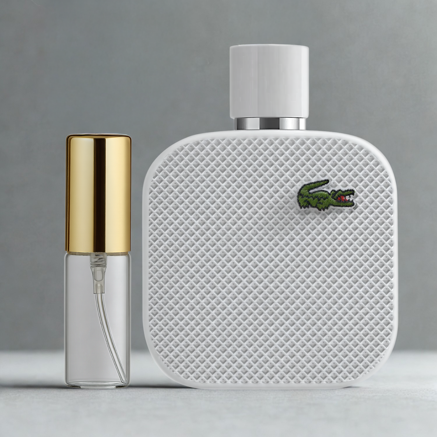 Decant de 5ml com borrifador dourado ao lado do frasco original do perfume importado masculino L.12.12 Blanc Lacoste Eau de Toilette, ambos sobre uma superfície e fundo cinza claro. A imagem destaca a apresentação do decant para venda e a familiaridade com o frasco original, disponíveis na Velyre.