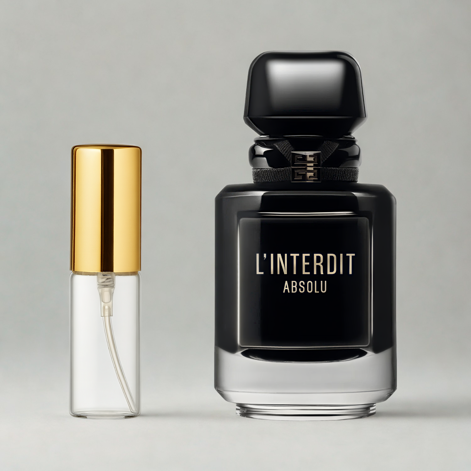 Decant de 5ml com borrifador dourado ao lado do frasco original do perfume importado feminino L'Interdit Absolu Givenchy Eau de Parfum Intense, ambos sobre uma superfície e fundo cinza claro. A imagem destaca a apresentação do decant para venda e a familiaridade com o frasco original, disponíveis na Velyre.