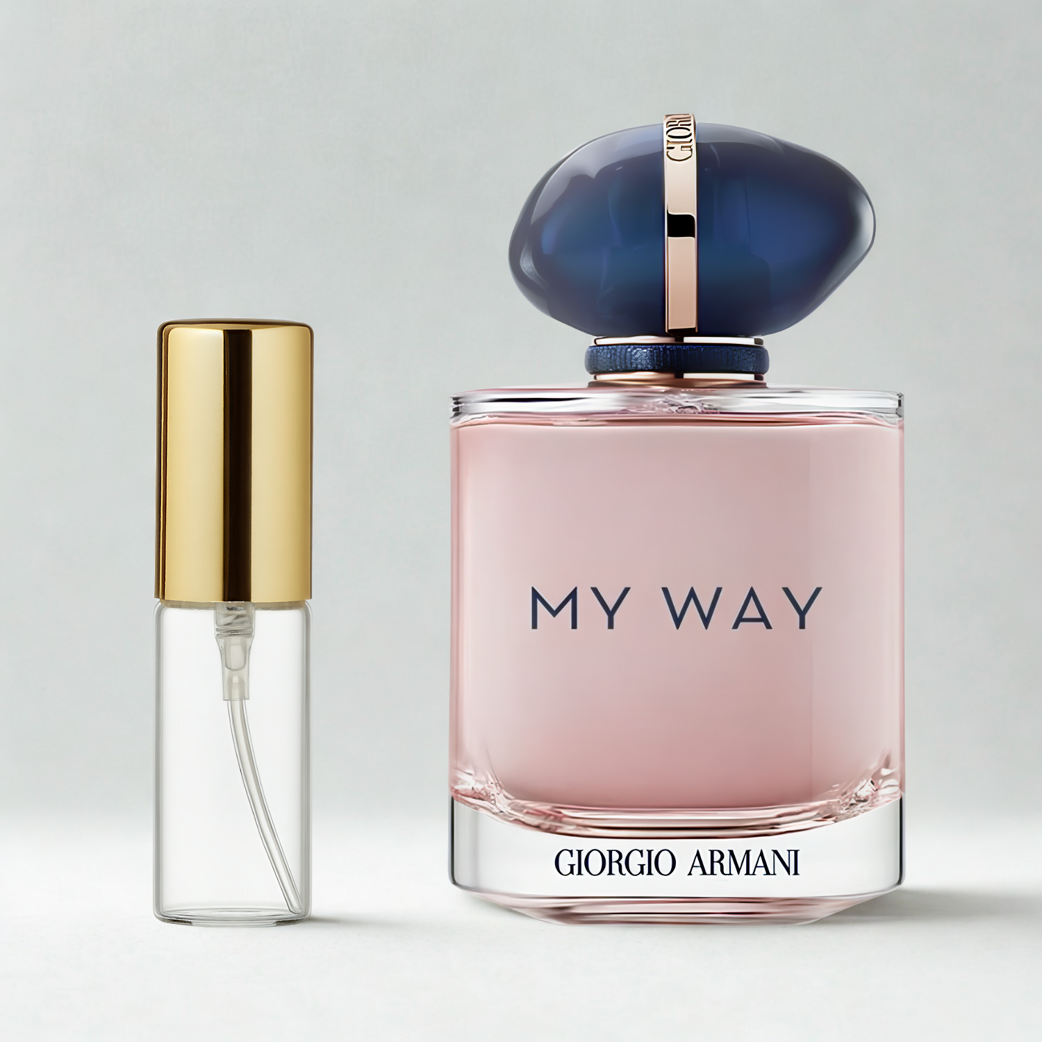 Decant de 5ml com borrifador dourado ao lado do frasco original do perfume importado feminino My Way Giorgio Armani Eau de Parfum, ambos sobre uma superfície e fundo cinza claro. A imagem destaca a apresentação do decant para venda e a familiaridade com o frasco original, disponíveis na Velyre.
