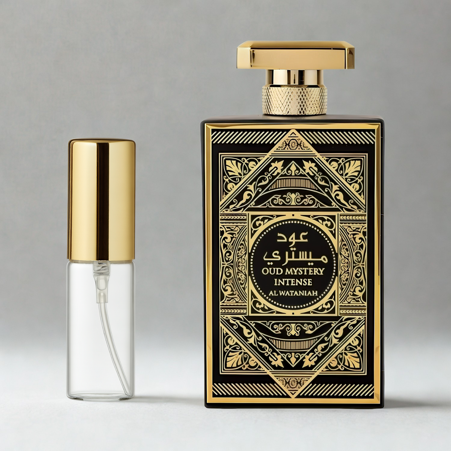 Decant de 5ml com borrifador dourado ao lado do frasco original do perfume árabe Oud Mystery Intense Al Wataniah Eau de Parfum, ambos sobre uma superfície e fundo cinza claro. A imagem destaca a apresentação do decant para venda e a familiaridade com o frasco original, disponíveis na Velyre.