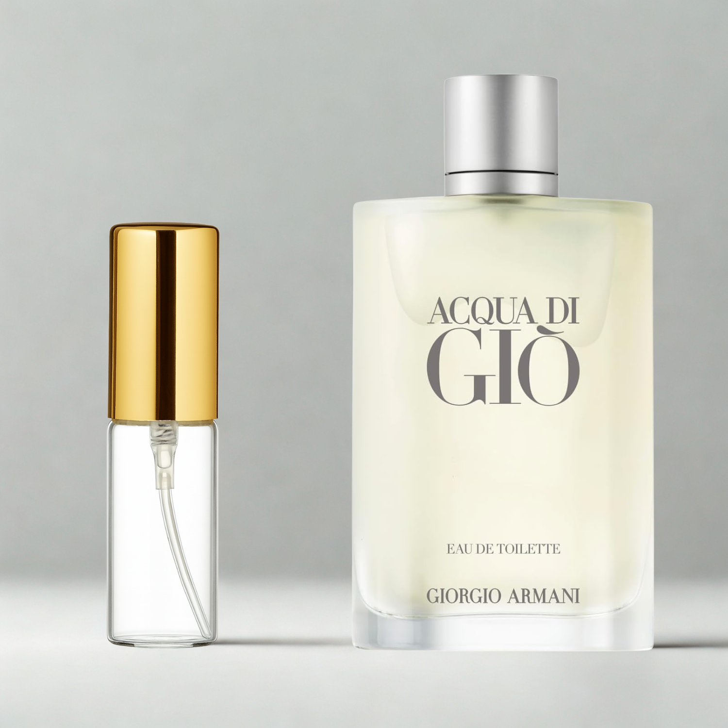 Decant de 5ml com borrifador dourado ao lado do frasco original do perfume importado masculino Acqua di Giò Giorgio Armani Eau de Toilette, ambos sobre uma superfície e fundo cinza claro. A imagem destaca a apresentação do decant para venda e a familiaridade com o frasco original, disponíveis na Velyre.