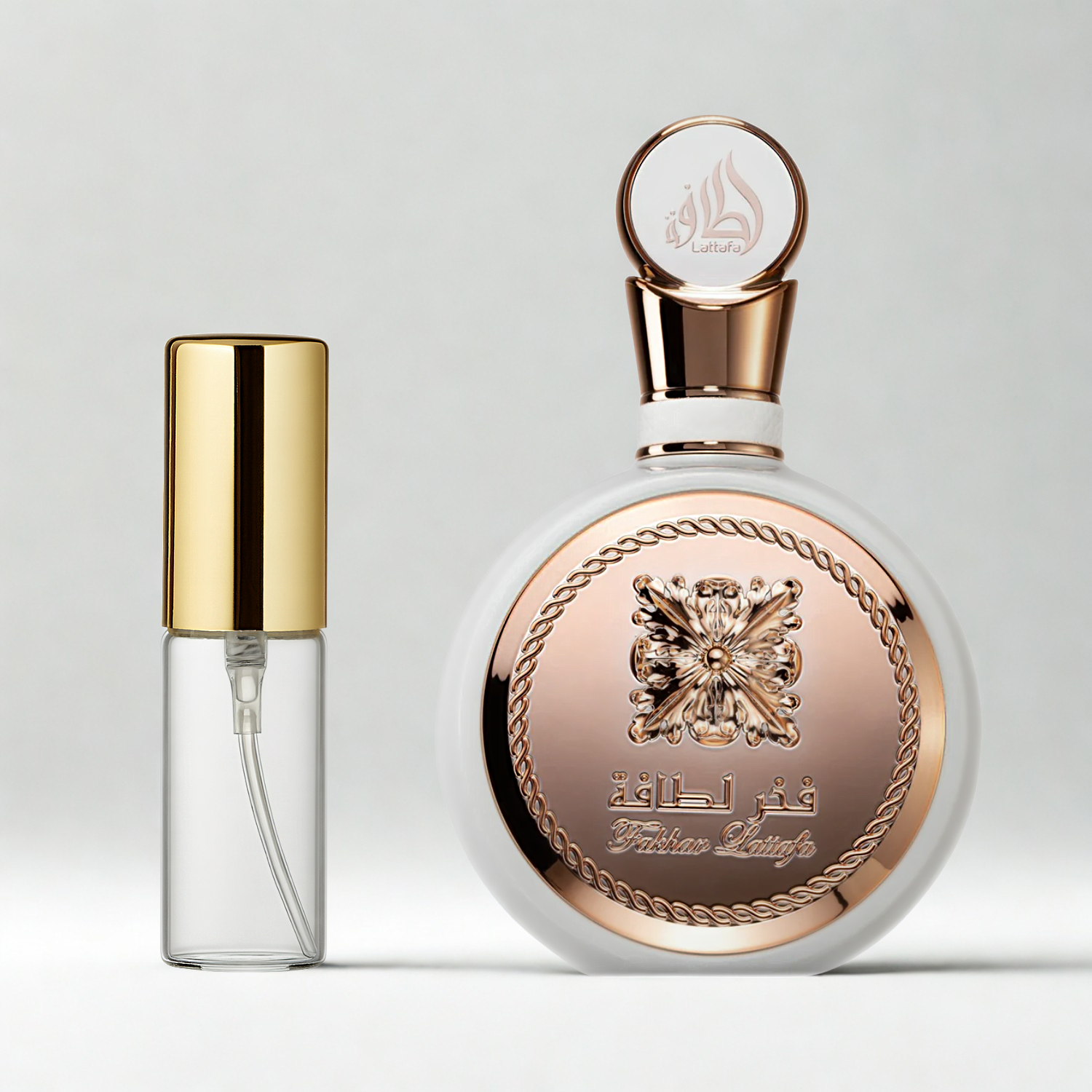 Decant de 5ml com borrifador dourado ao lado do frasco original do perfume árabe feminino Fakhar Rose Lattafa Eau de Parfum, ambos sobre uma superfície e fundo cinza claro. A imagem destaca a apresentação do decant para venda e a familiaridade com o frasco original, disponíveis na Velyre.