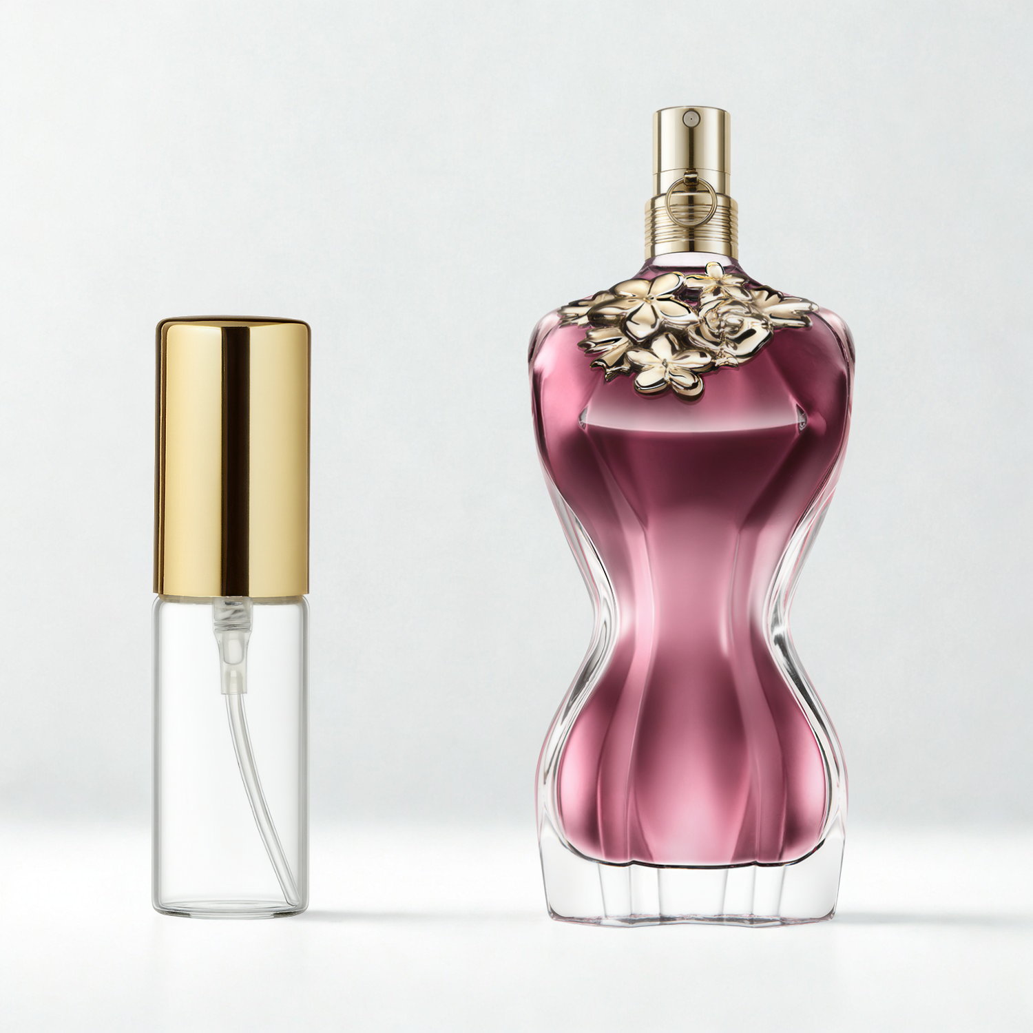 Decant de 5ml com borrifador dourado ao lado do frasco original do perfume importado feminino La Belle Jean Paul Gaultier Eau de Parfum, ambos sobre uma superfície e fundo cinza claro. A imagem destaca a apresentação do decant para venda e a familiaridade com o frasco original, disponíveis na Velyre.