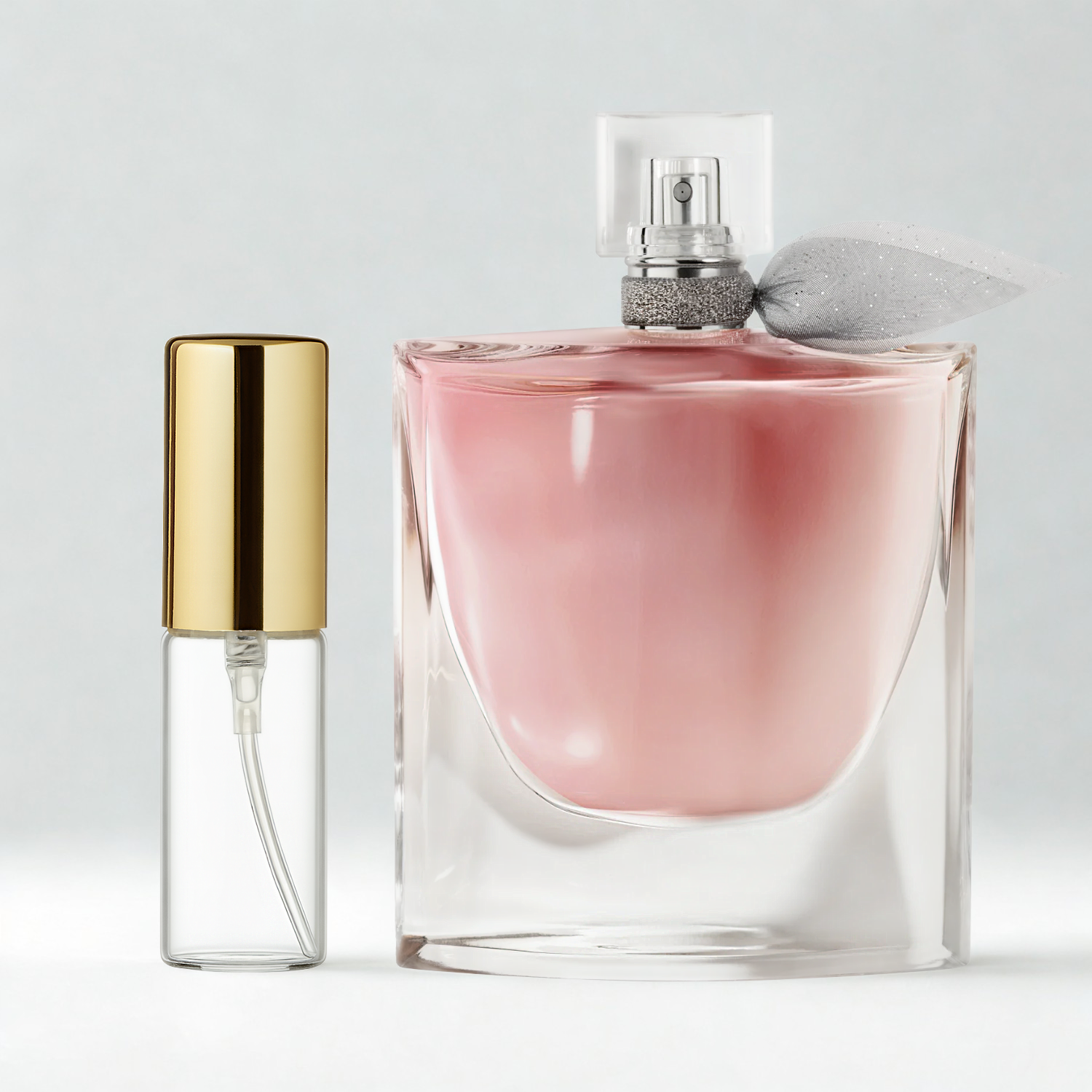 Decant de 5ml com borrifador dourado ao lado do frasco original do perfume importado feminino La Vie Est Belle Lancôme Eau de Parfum, ambos sobre uma superfície e fundo cinza claro. A imagem destaca a apresentação do decant para venda e a familiaridade com o frasco original, disponíveis na Velyre.