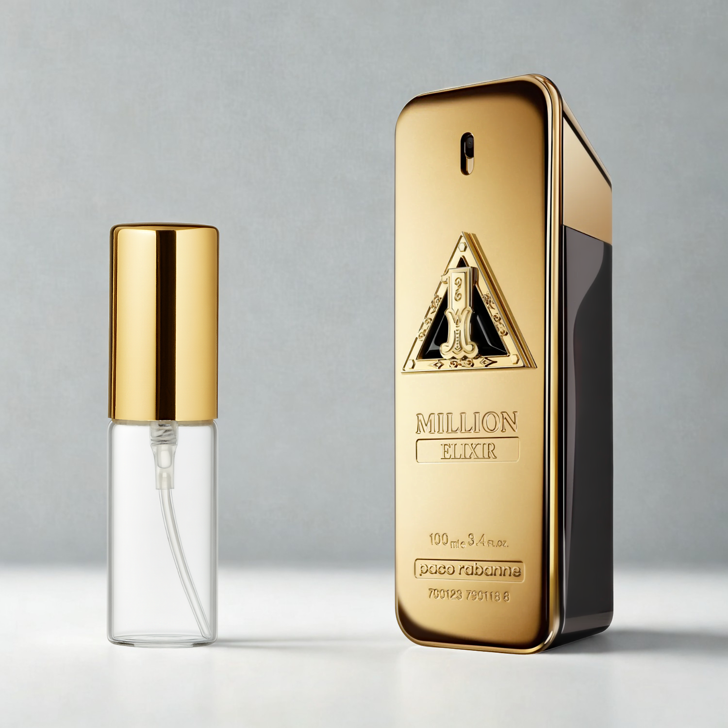 Decant de 5ml com borrifador dourado ao lado do frasco original do perfume importado masculino One Million Elixir Rabanne Eau de Parfum, ambos sobre uma superfície e fundo cinza claro. A imagem destaca a apresentação do decant para venda e a familiaridade com o frasco original, disponíveis na Velyre.