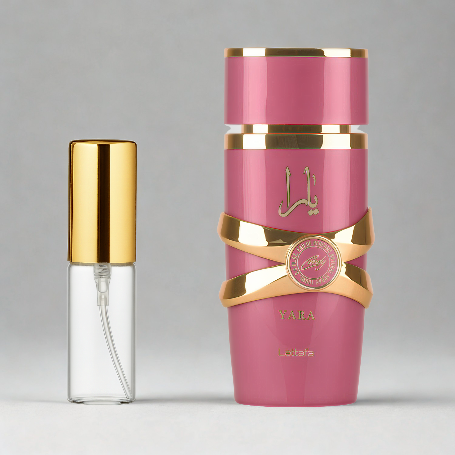 Decant de 5ml com borrifador dourado ao lado do frasco original do perfume árabe feminino Yara Candy Lattafa Eau de Parfum, ambos sobre uma superfície e fundo cinza claro. A imagem destaca a apresentação do decant para venda e a familiaridade com o frasco original, disponíveis na Velyre.