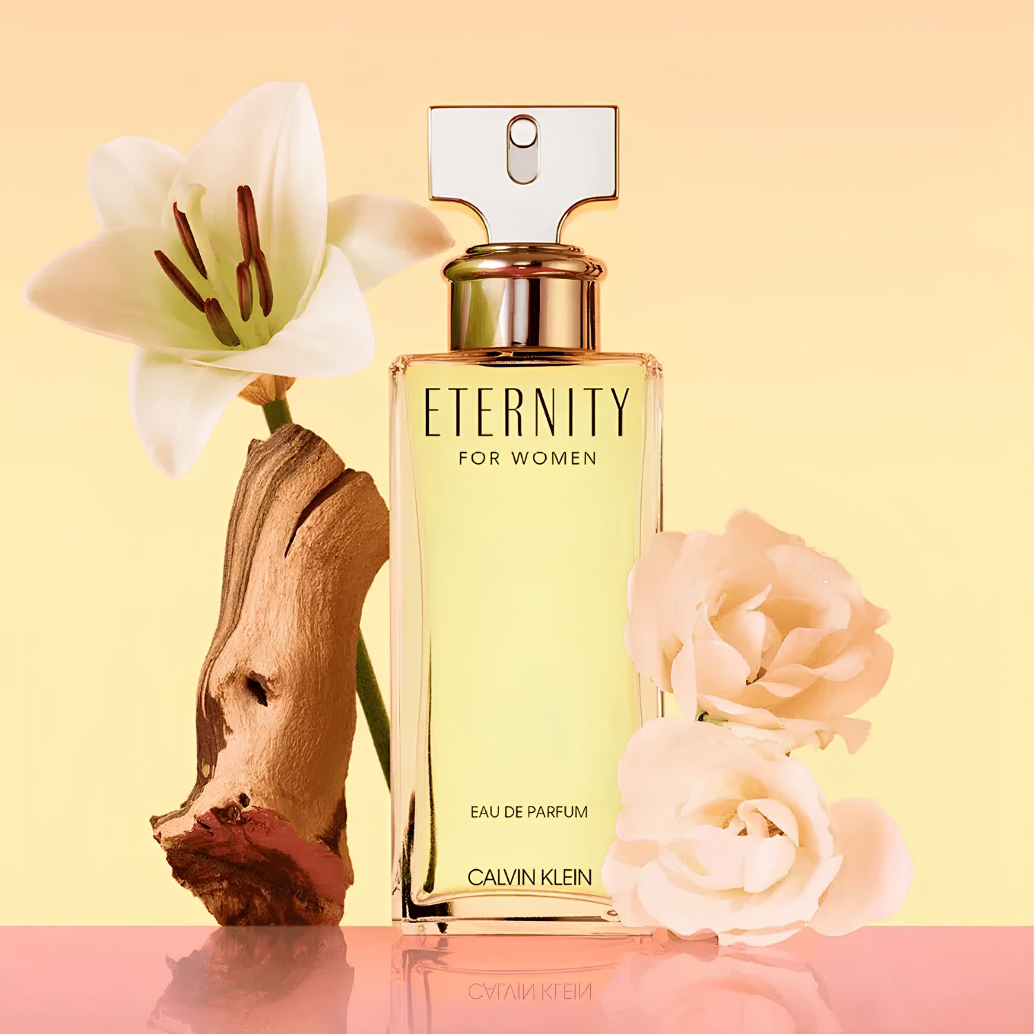 Perfume feminino Eternity for Women Calvin Klein em destaque em uma composição suave com um lírio branco elegante, rosas claras e um pedaço de madeira clara texturizada, sobre um fundo em tons de pêssego e rosa, evocando uma fragrância floral delicada e atemporal.