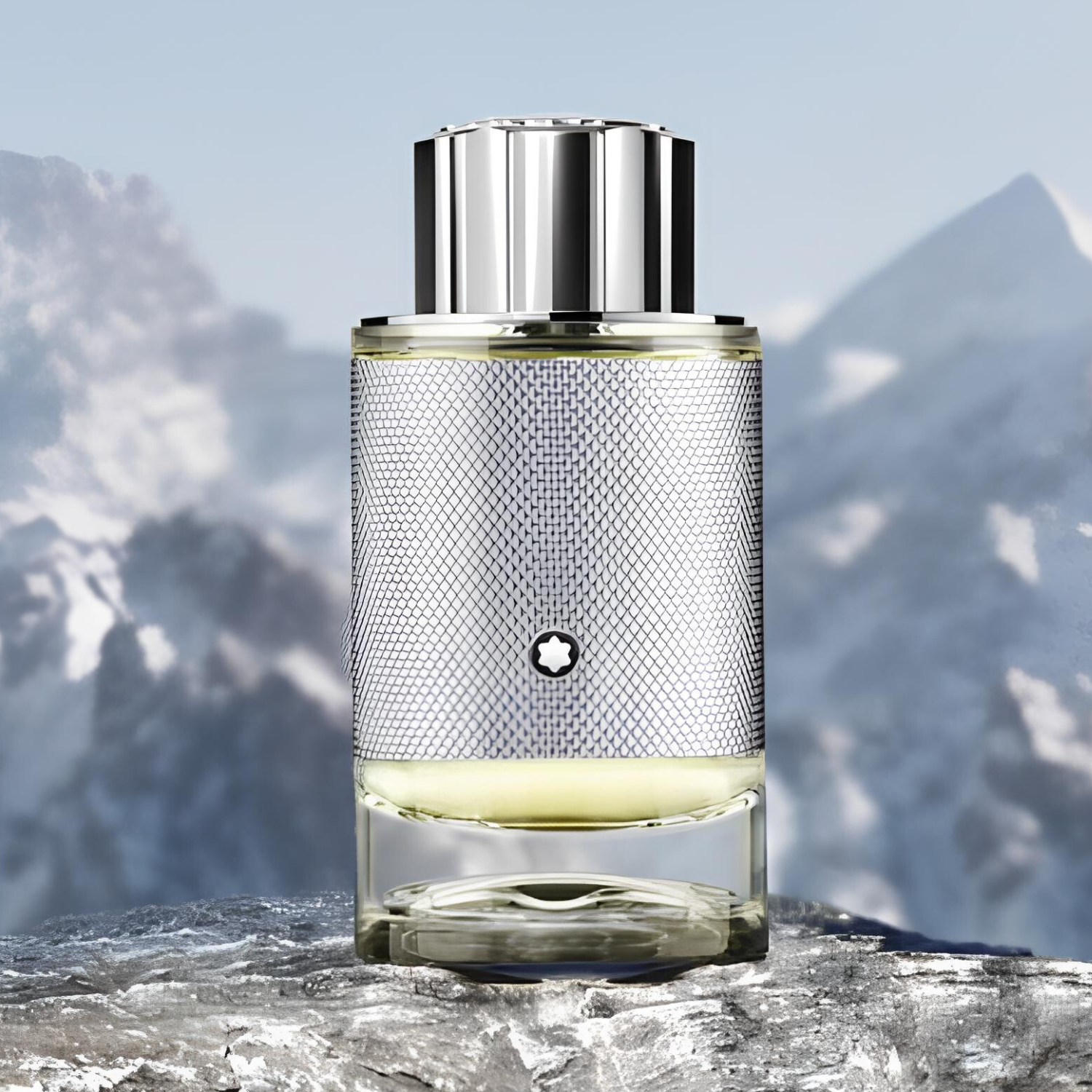 Montblanc Explorer Platinum posicionado sobre uma rocha com fundo de montanhas desfocadas. O frasco tem corpo metálico texturizado e tampa prateada reluzente, transmitindo uma sensação de frescor e altitude.