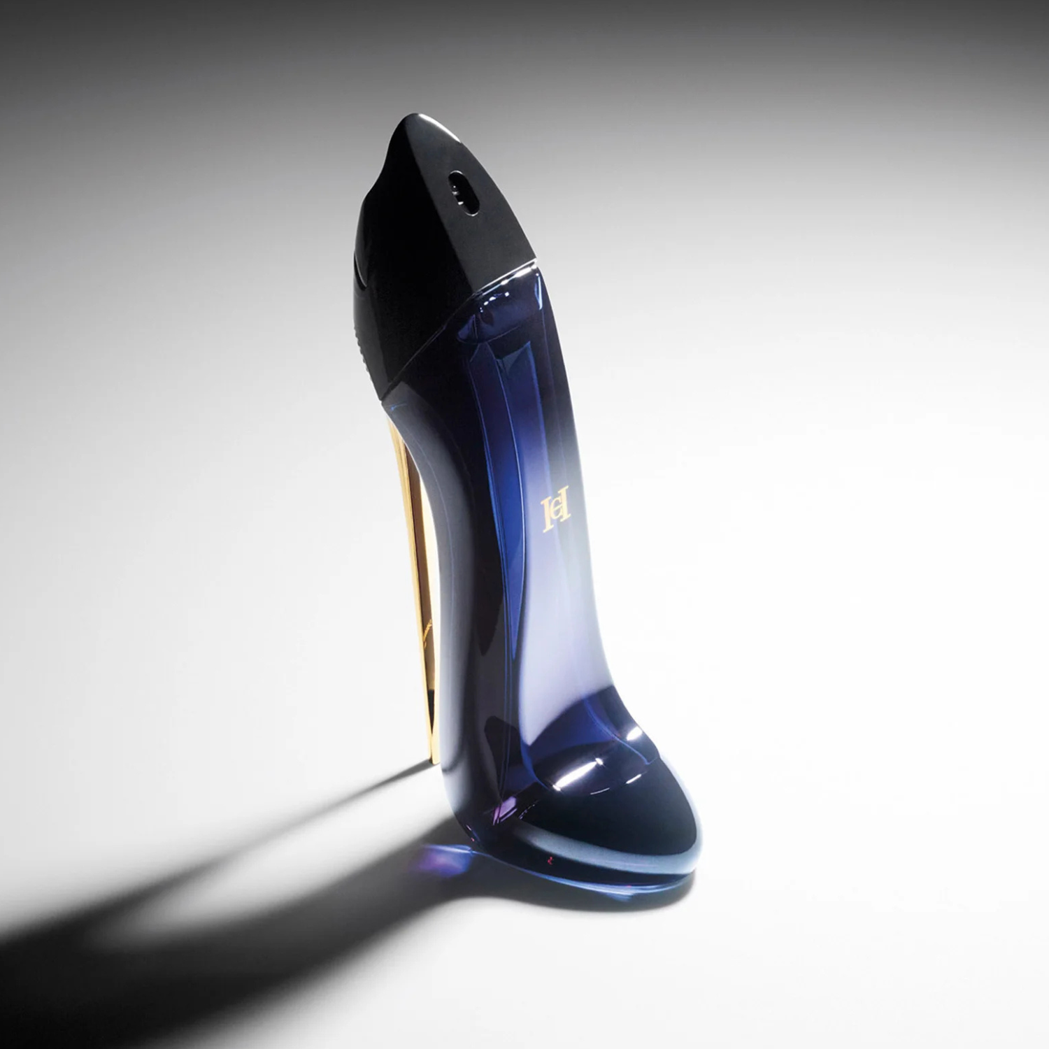 Perfume Good Girl Carolina Herrera inclinado sobre um fundo claro com uma sombra bem definida, realçando o design escultural do frasco em formato de sapato e a combinação de cores azul e dourado.