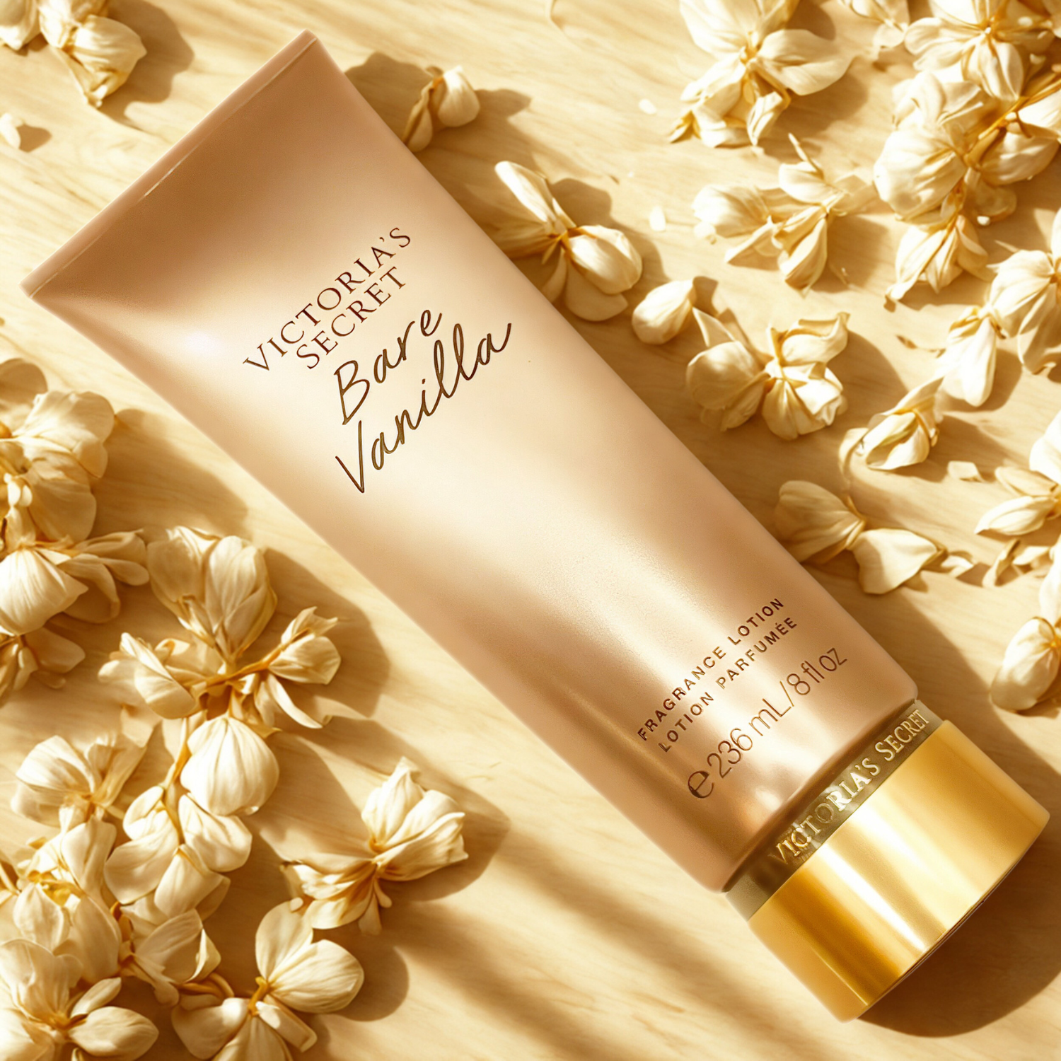 Tubo do hidratante perfumado importado Bare Vanilla Victoria's Secret em destaque sobre uma superfície bege, com folhagens secas em tons claros ao redor, evocando um aroma de baunilha suave e natural, disponível na Velyre.