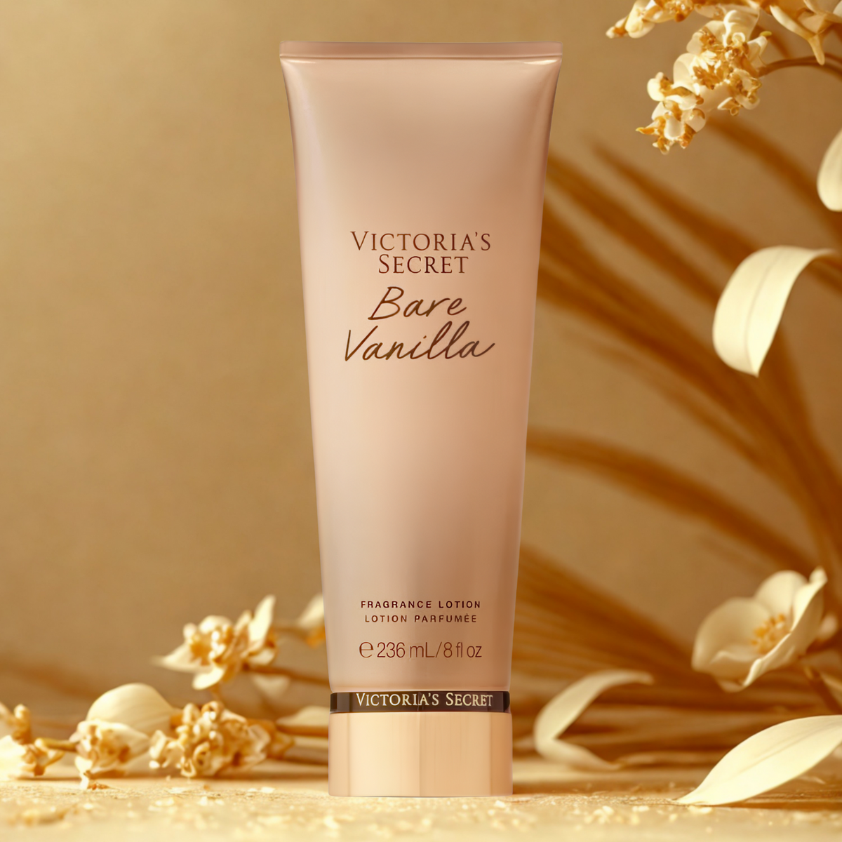 Tubo do hidratante perfumado importado Bare Vanilla Victoria's Secret inclinado sobre uma superfície em tons dourados, rodeado por flores secas claras, transmitindo uma sensação de delicadeza e um aroma doce e aconchegante, disponível na Velyre.