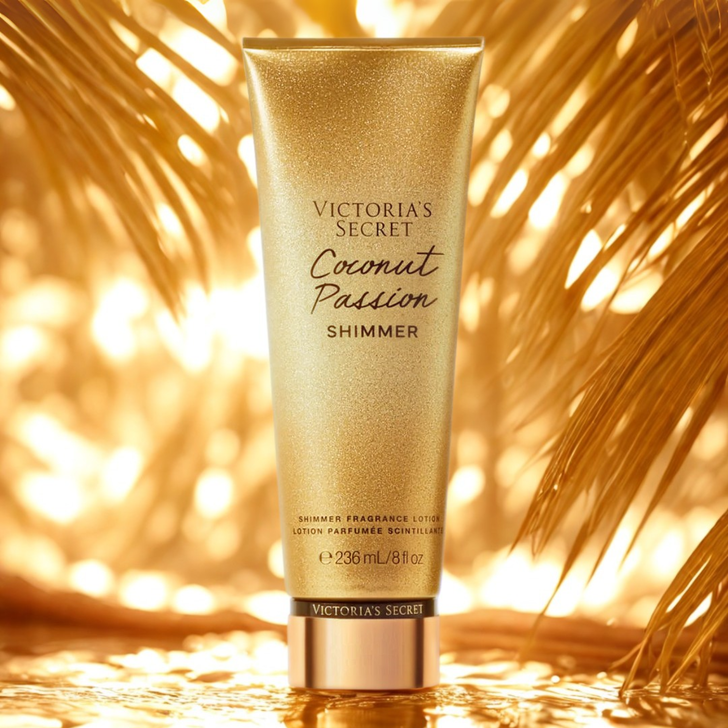 Tubo do hidratante perfumado importado Coconut Passion Shimmer Victoria's Secret em destaque em um ambiente tropical com folhas de palmeira douradas ao fundo, evocando uma fragrância exótica e luminosa, disponível na Velyre.