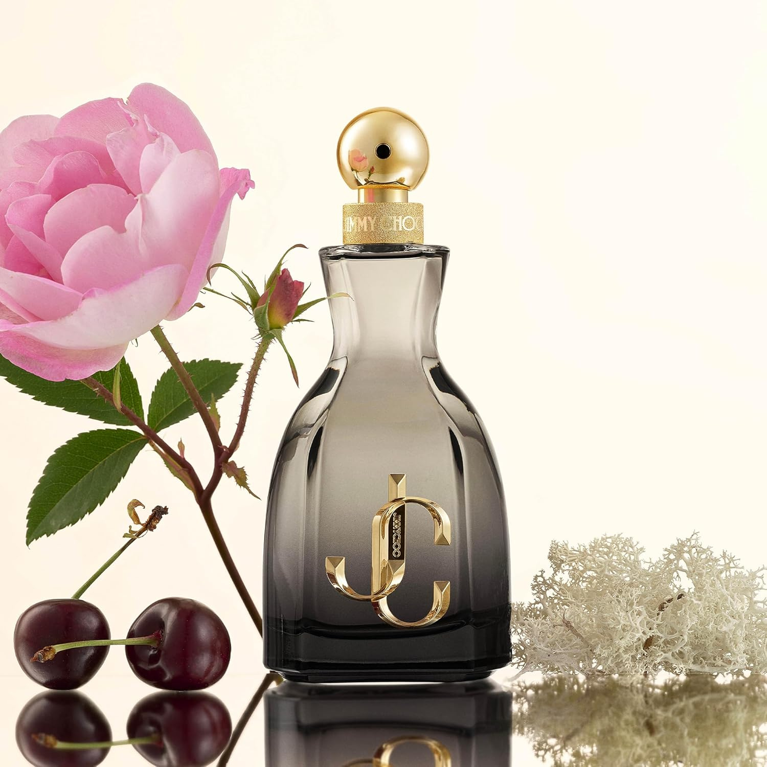 Perfume feminino I Want Choo Forever Jimmy Choo em destaque ao lado de uma rosa rosa, cerejas vermelhas e musgo branco, sobre um fundo claro, sugerindo uma fragrância floral frutada com um toque elegante e duradouro.