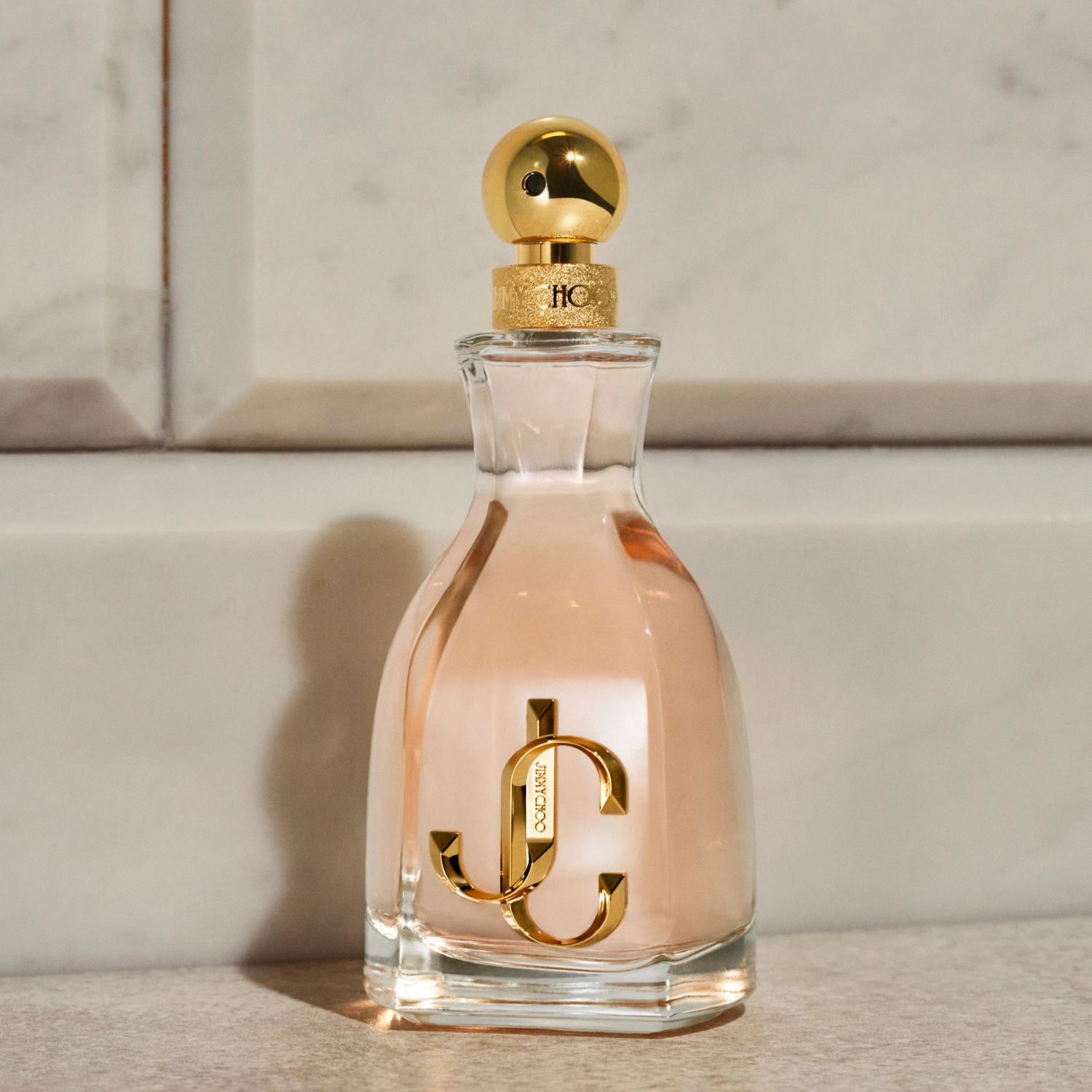 Perfume feminino I Want Choo Jimmy Choo em destaque sobre um fundo neutro com textura sutil, realçando as curvas do frasco e o brilho do logo dourado.