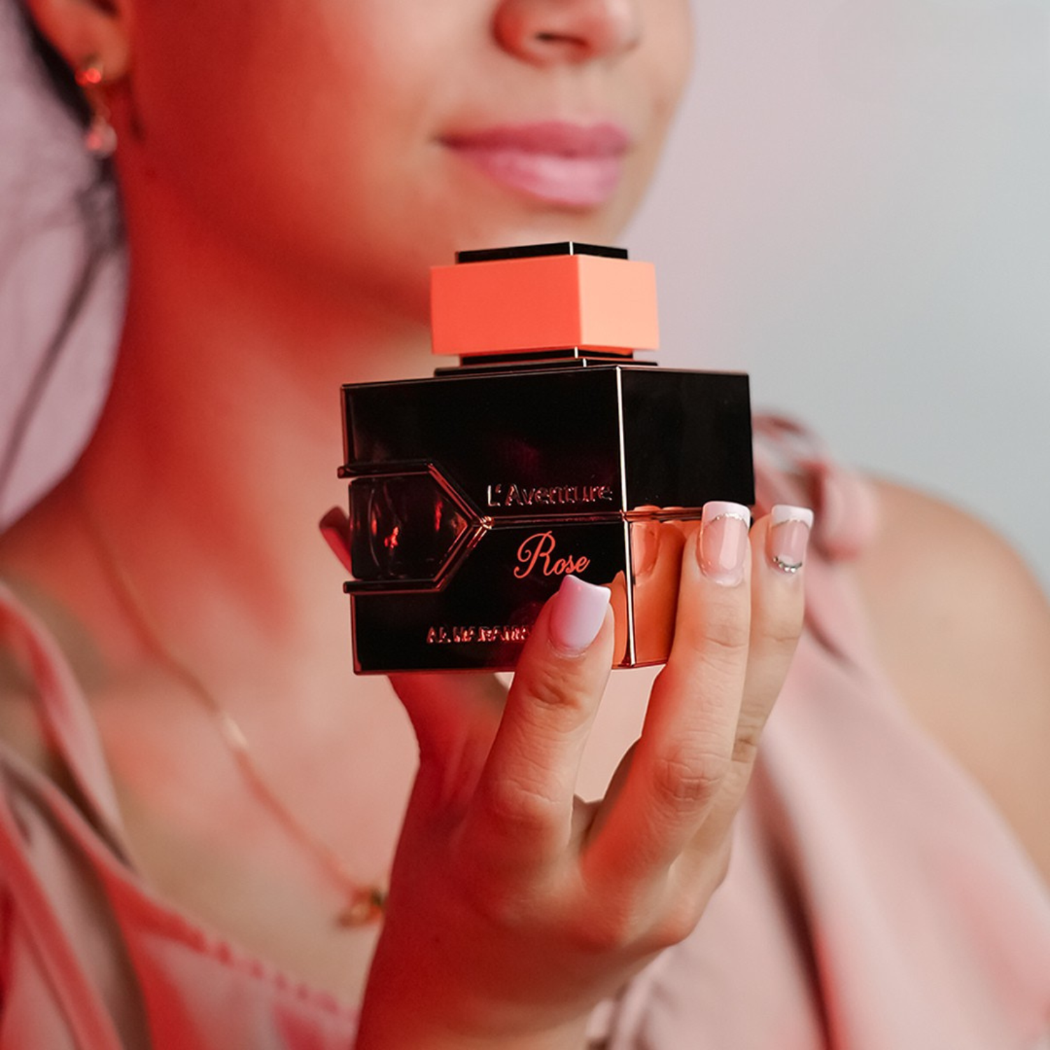 Close-up de uma mulher segurando o perfume árabe L'aventure Rose Al Haramain, disponível na Velyre, com foco no frasco e nas mãos delicadas, sugerindo fragrância feminina e elegante.