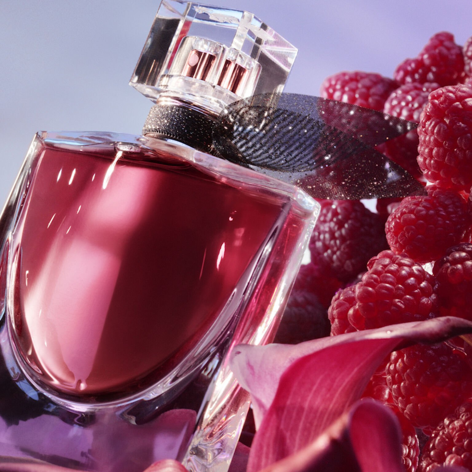Close-up do perfume La Vie Est Belle L'Elixir Lancôme cercado por framboesas maduras e pétalas de flores rosa, sugerindo notas frutadas e florais da fragrância em um fundo azul suave.