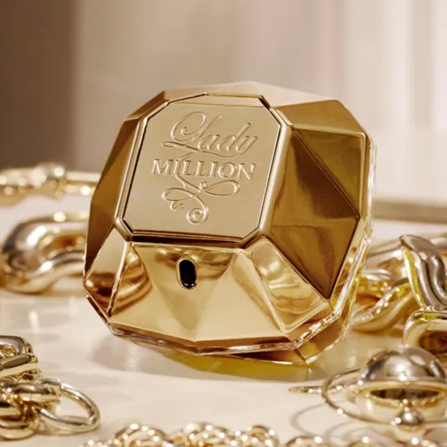 Perfume importado feminino Lady Million Rabanne em destaque sobre uma superfície clara, cercado por diversas joias e acessórios dourados, evocando luxo e riqueza, disponível na Velyre.