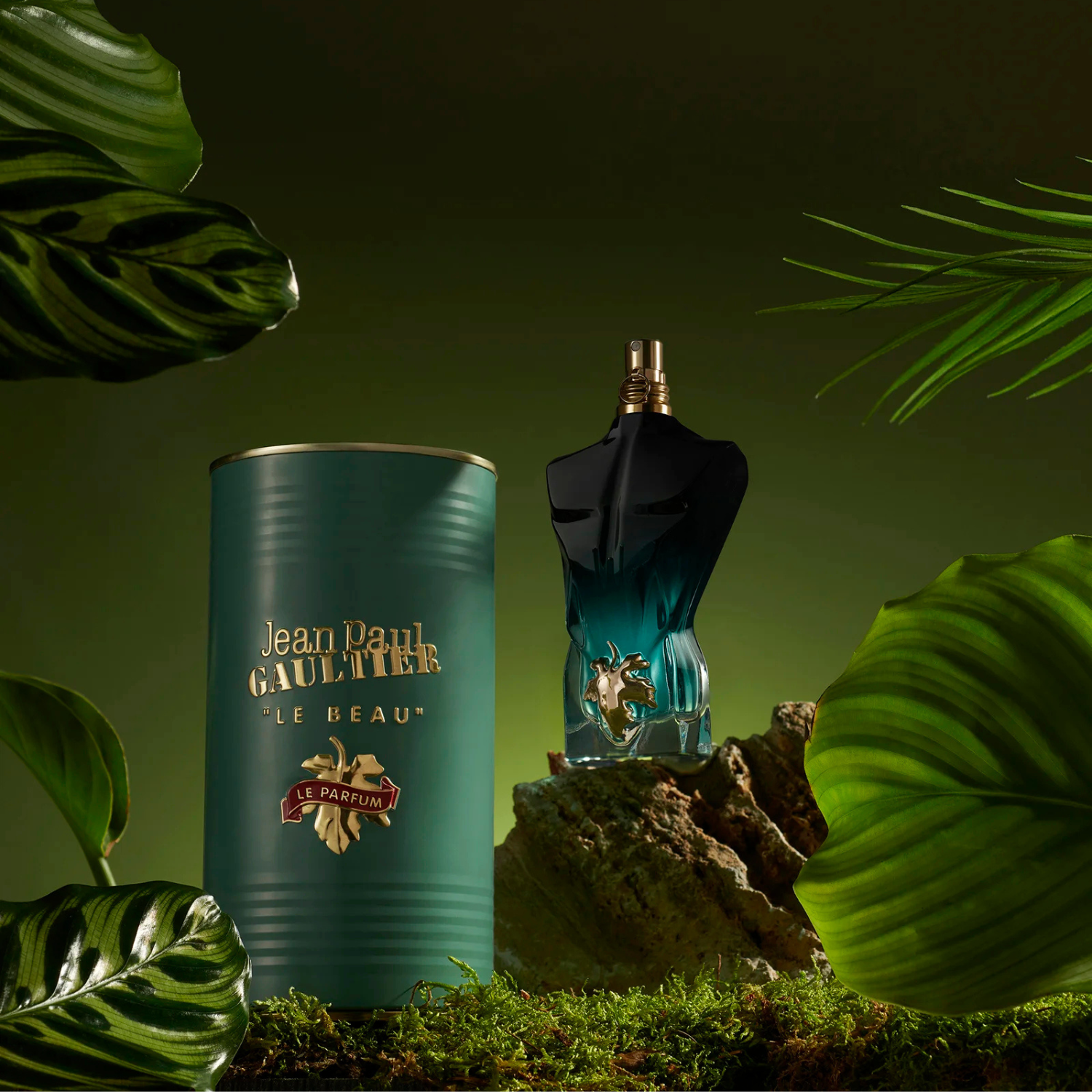 Perfume Le Beau Le Parfum Jean Paul Gaultier ao lado de sua embalagem em formato de lata verde escura, em um ambiente natural com musgo e rochas, destacando a apresentação completa do produto e seu tema tropical.