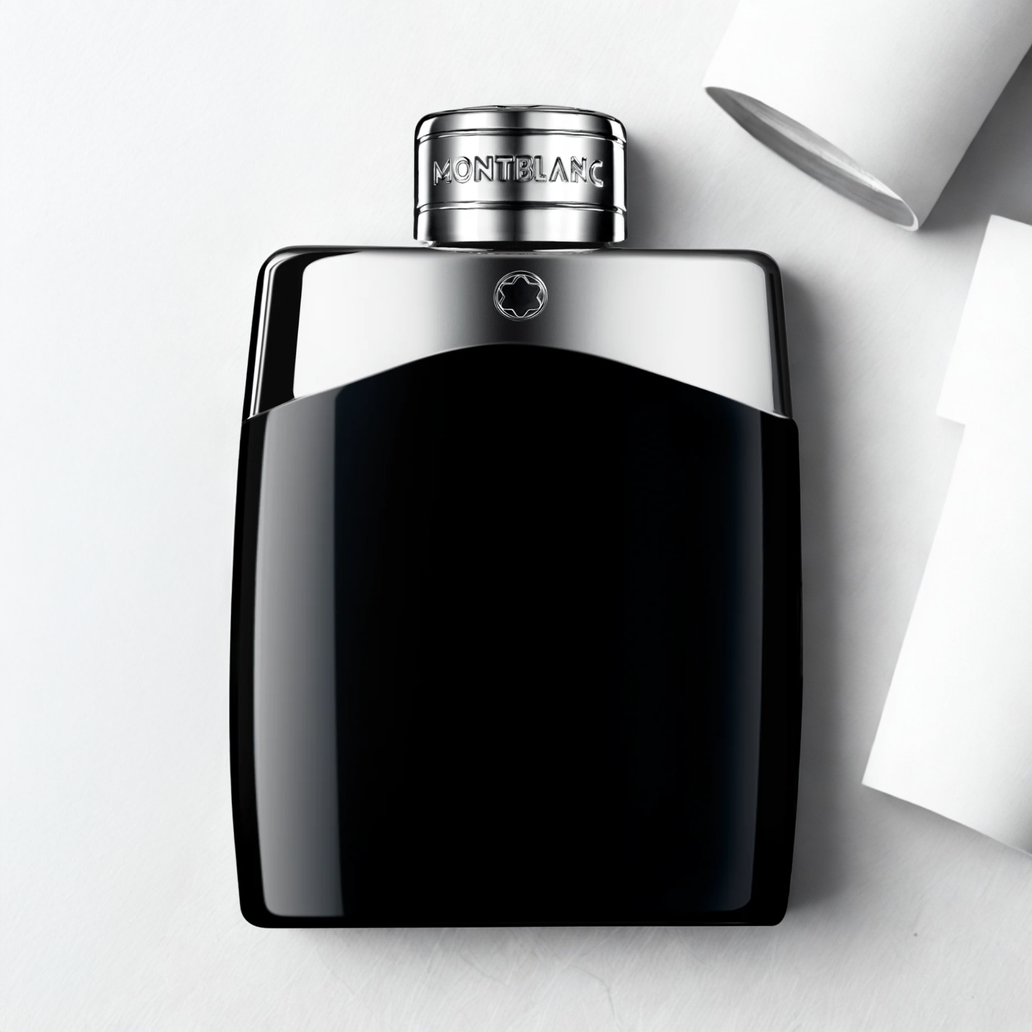 Frasco do Montblanc Legend sobre fundo branco com objetos de papel ao redor, destacando o contraste sofisticado.