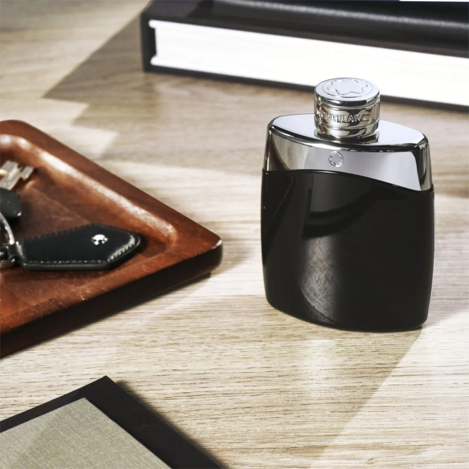 Perfume Montblanc Legend sobre mesa de madeira com chaves e livro, transmitindo elegância e estilo masculino clássico.